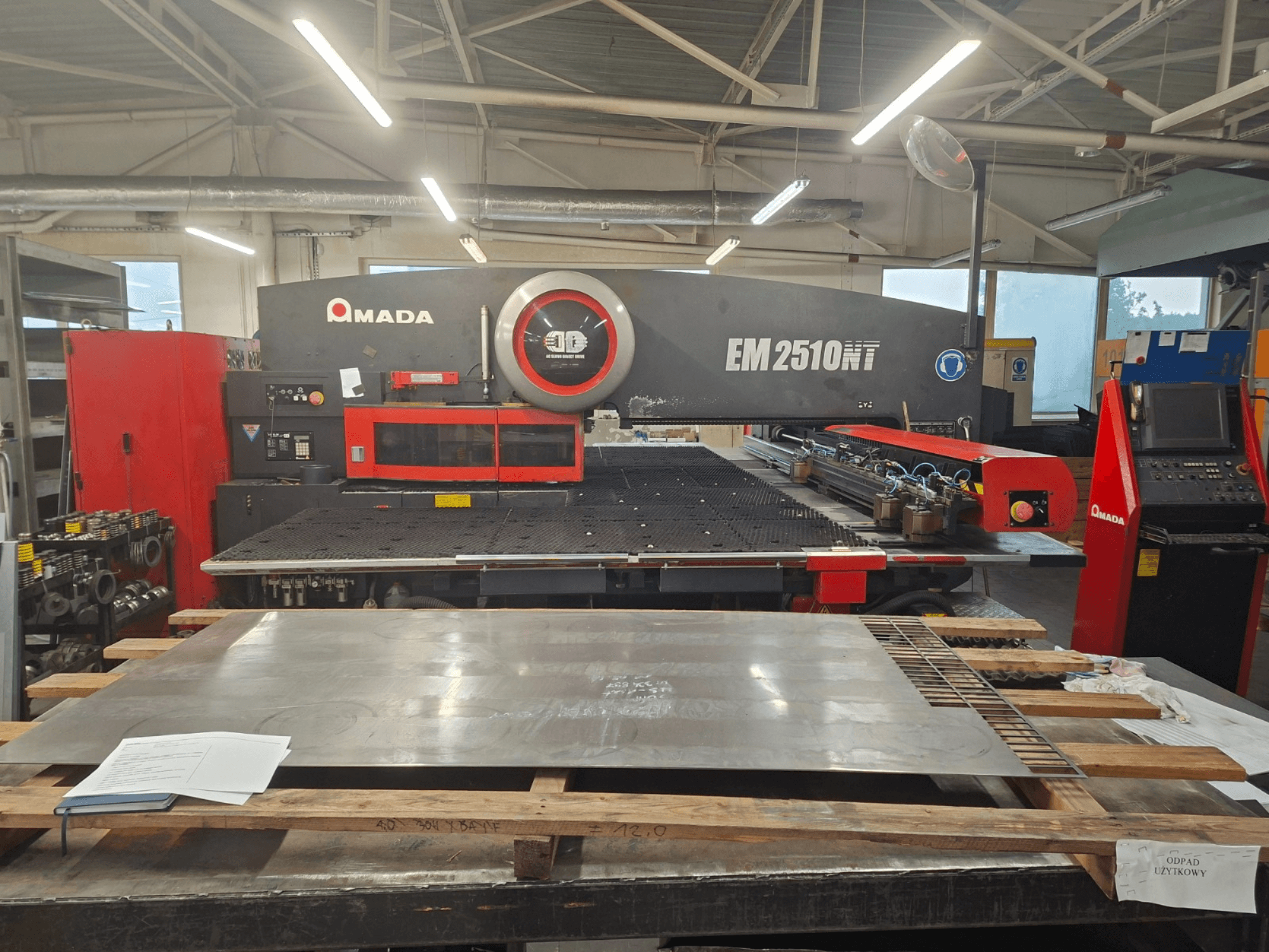 AMADA EM 2510NT bokštelinio perforatoriaus vaizdas iš priekio, dirbtuvėse matomas metalo lakštas ir valdymo skydelis.