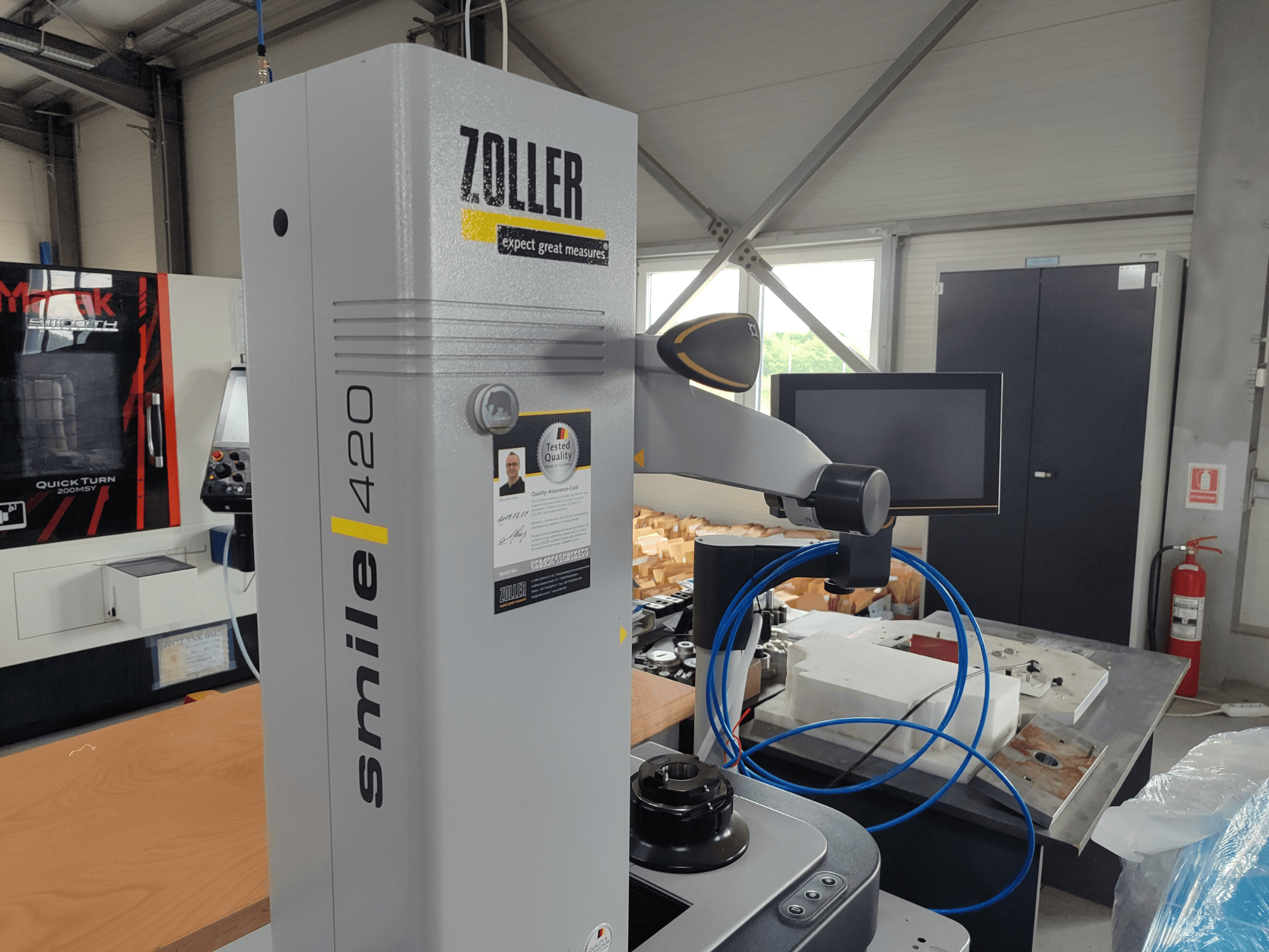 ZOLLER smile 420 matavimo prietaisas su monitoriumi, šoninis vaizdas dirbtuvėse, mėlynų žarnų ir mašinų fone.