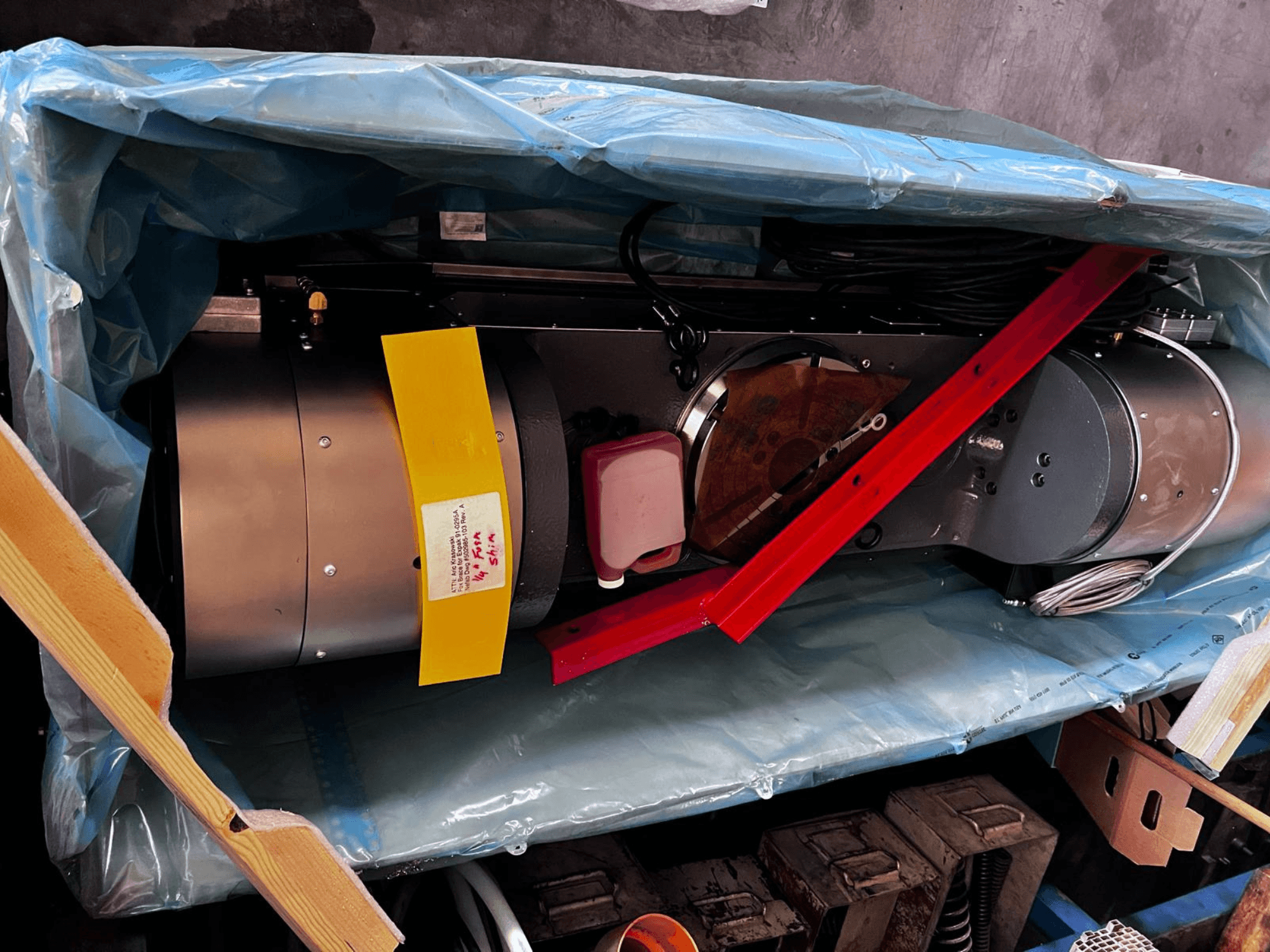 Variklio įtaisas iš dalies matomas pakuotėje, turi sidabrinę išorę, spalvotus matuoklius ir raudoną atraminę apkabą.