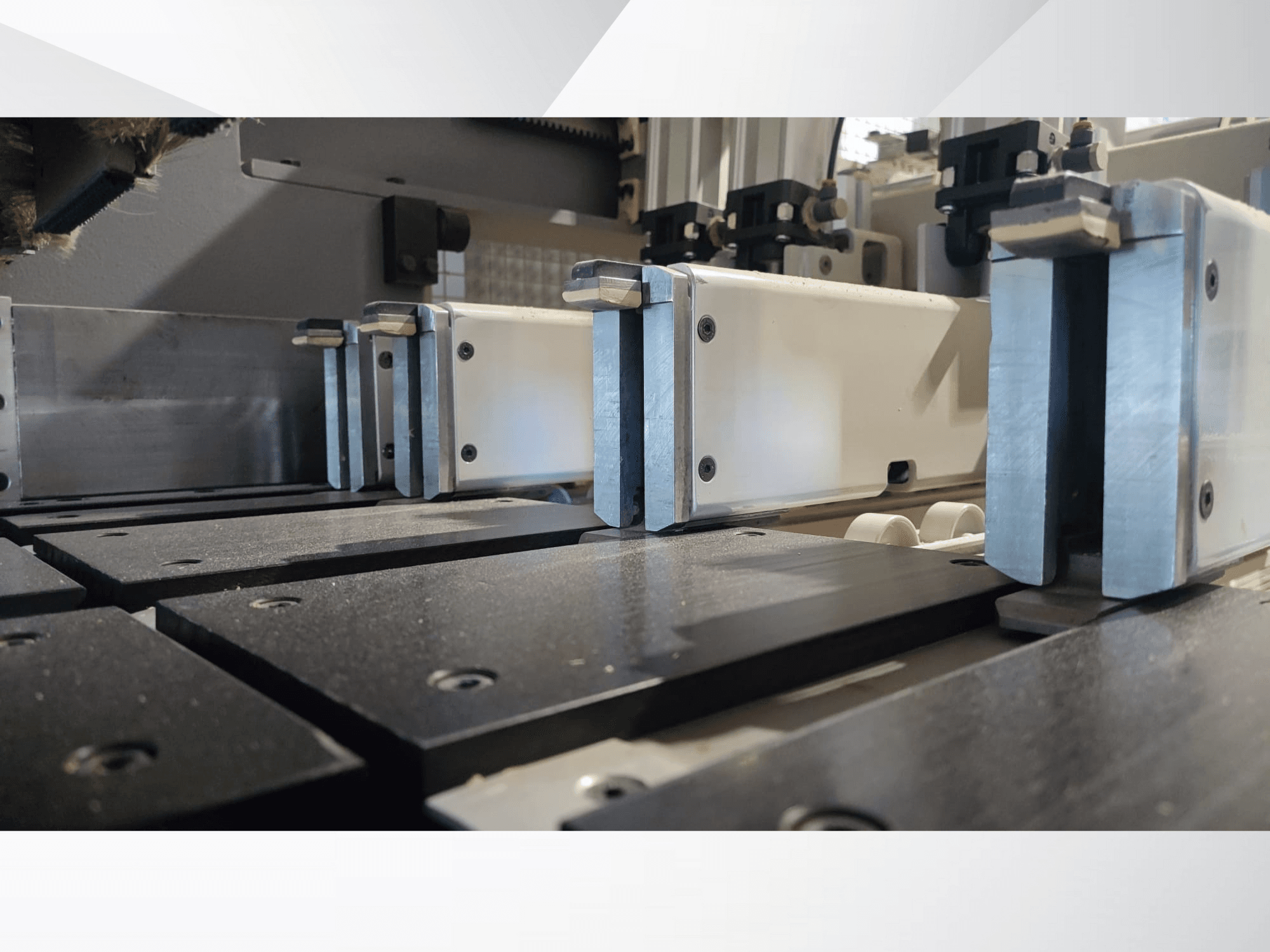 Precizinių staklių su metalinėmis žandikauliais, juodais darbiniais paviršiais ir matomais kreipiamaisiais bėgeliais prispaudimo mechanizmo vaizdas iš arti.