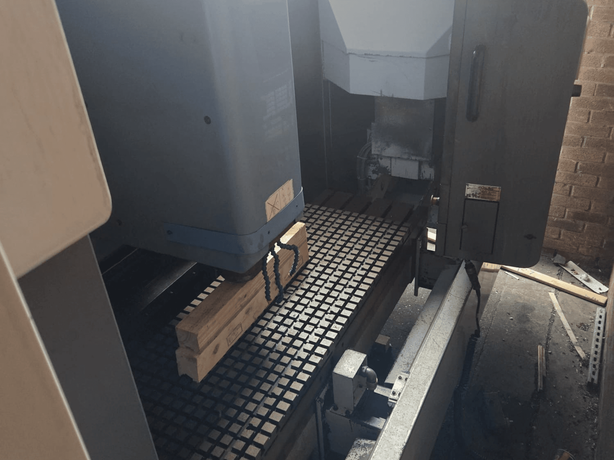 CNC staklių vaizdas iš priekio su medinėmis lentomis ant tinklelio stalo, šone matomi įrankiai ir valdikliai.