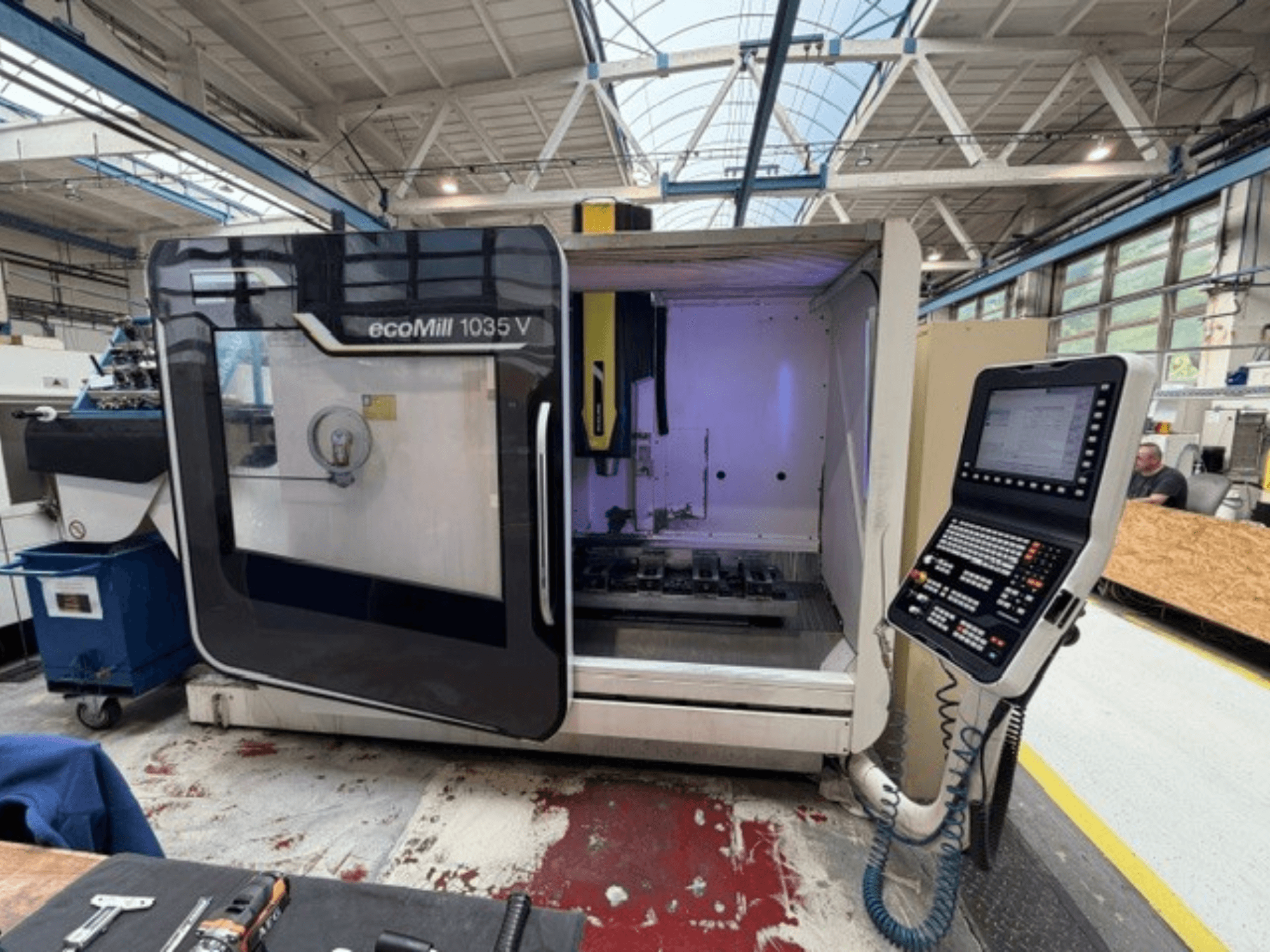 DMG MORI „ecoMill 1035V“ vertikaliojo apdirbimo centro vaizdas iš priekio su atidarytomis durimis, kuriame matomas valdymo pultas ir darbo zona viduje.