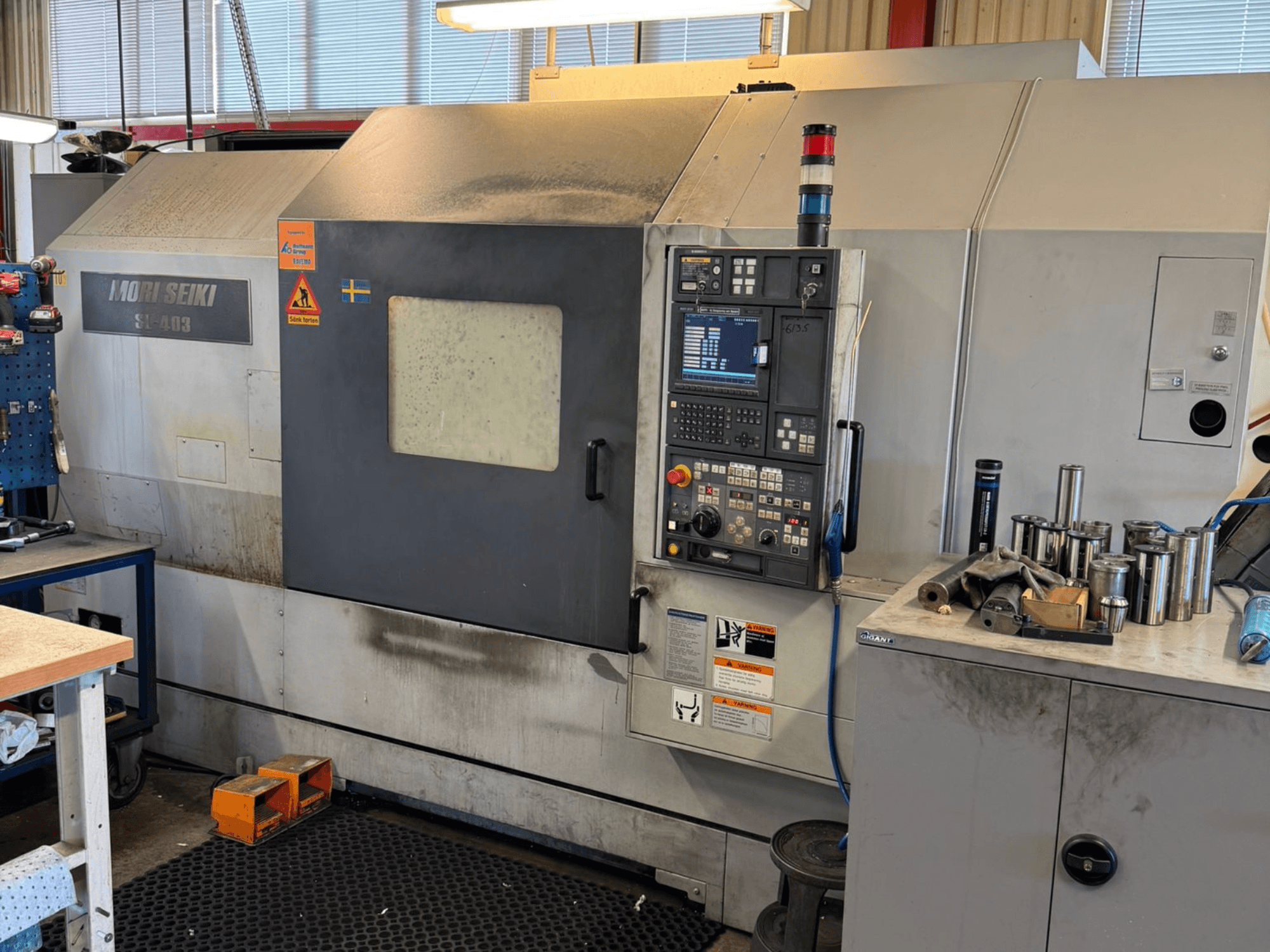 MORI SEIKI SL-403BMC/800 horizontalios tekinimo staklės dirbtuvėse, matomas valdymo skydelis ir šalia esantys įrankiai, vaizdas iš šono.