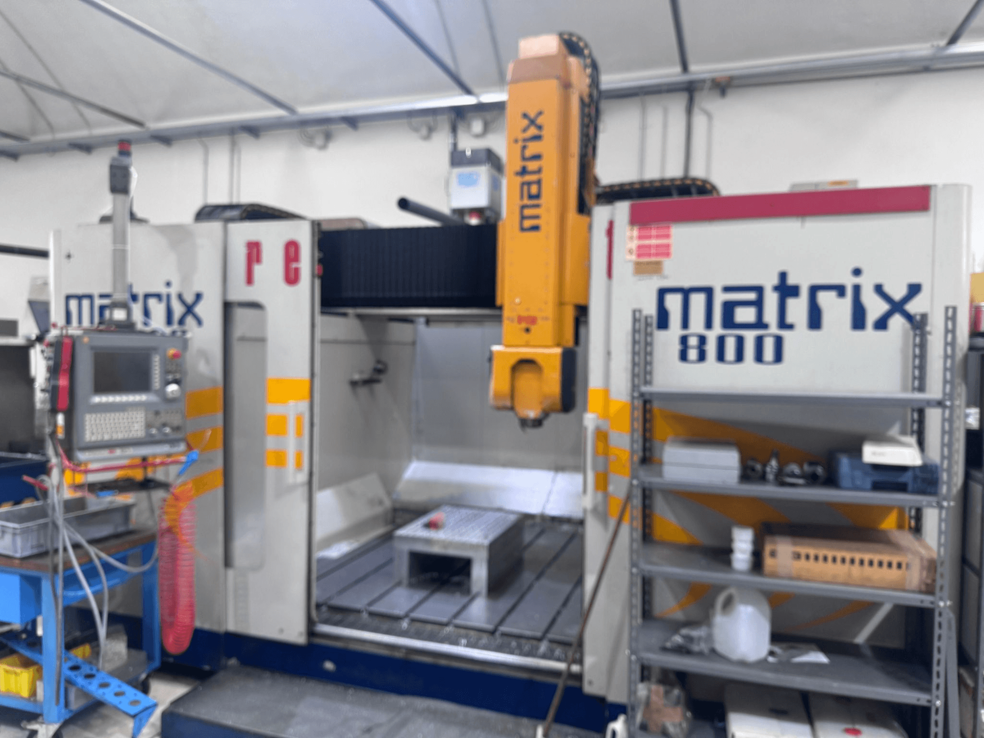 Matrix 800 CNC staklės dirbtuvėse, su valdymo pultu, įrankiais ir darbo stalu su įvairiais objektais.
