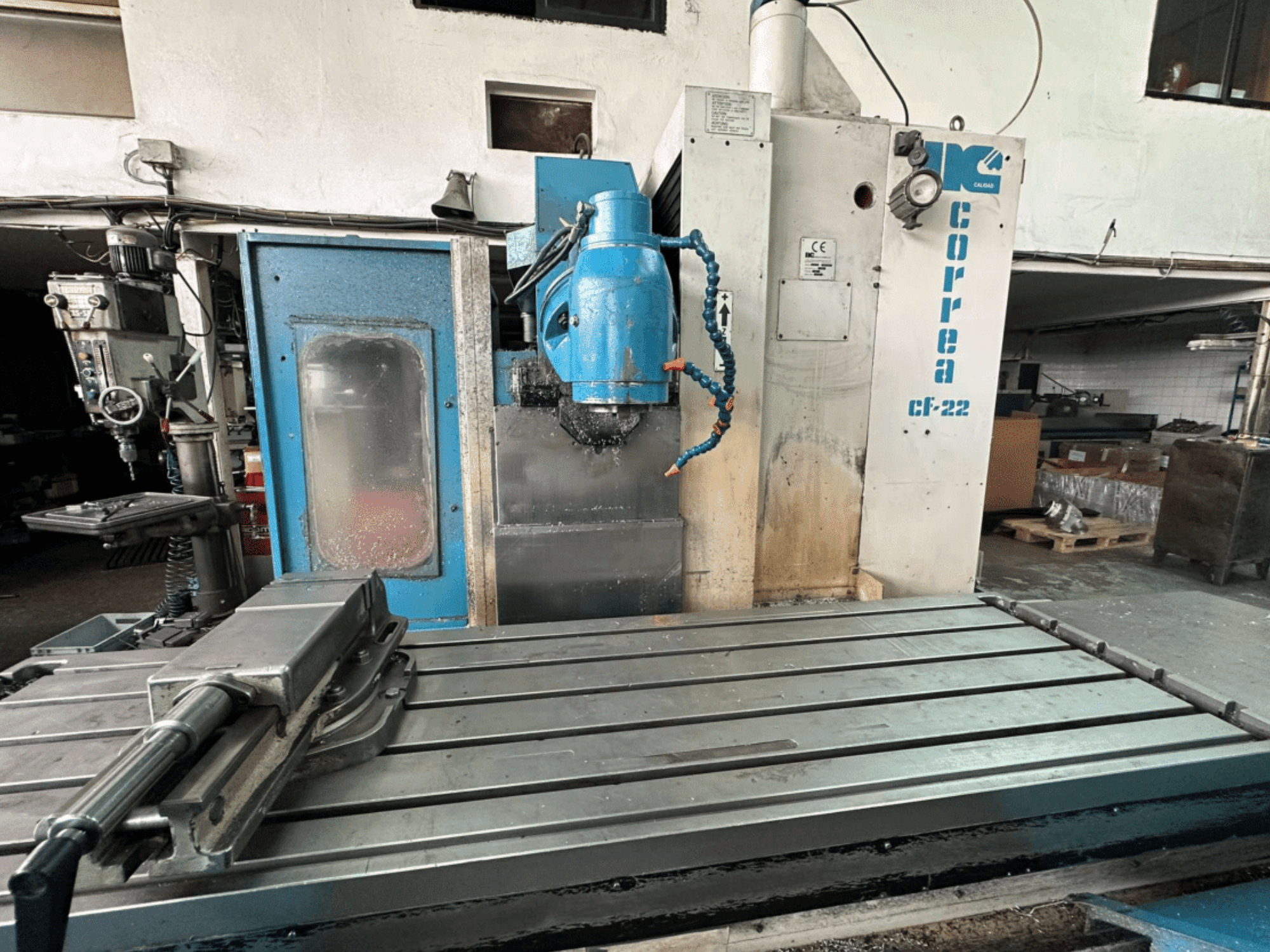 Mėlynos ir sidabrinės spalvos frezavimo staklės "Correa CF-22" su stumdomu stalu ir pjovimo galvute, parodytos iš priekio.