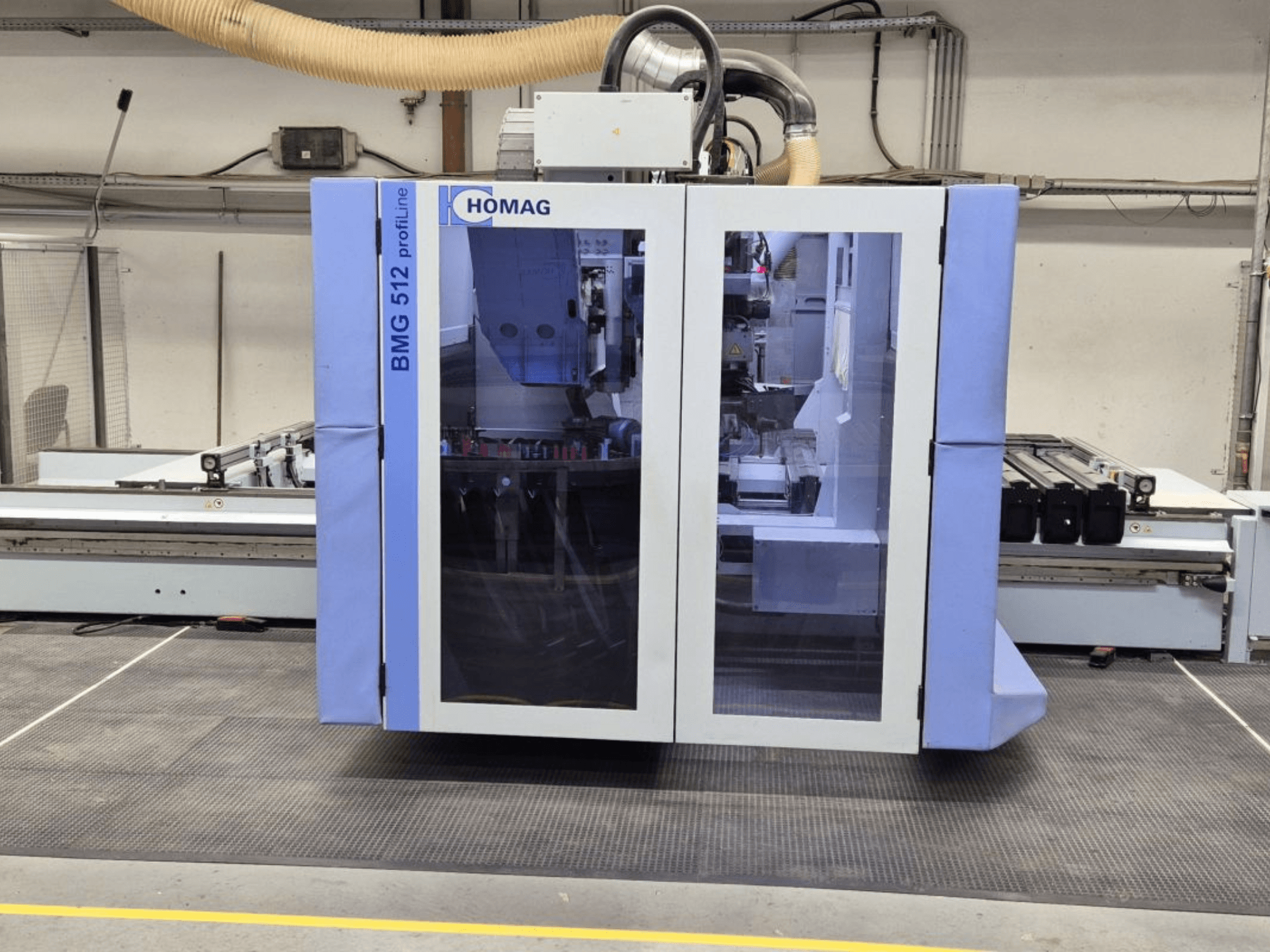 HOMAG BMG 512 ProfiLine CNC staklės, vaizdas iš priekio, stiklinis skydelis, matomi tikslūs įrankiai ir pramoninė aplinka.