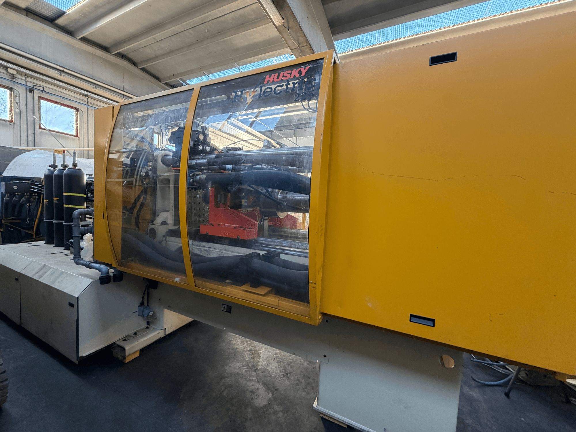 "Husky HL225 RS65" elektrinė įpurškimo mašina, vaizdas iš priekio, geltonas korpusas, matomas valdymo skydelis ir hidrauliniai komponentai.