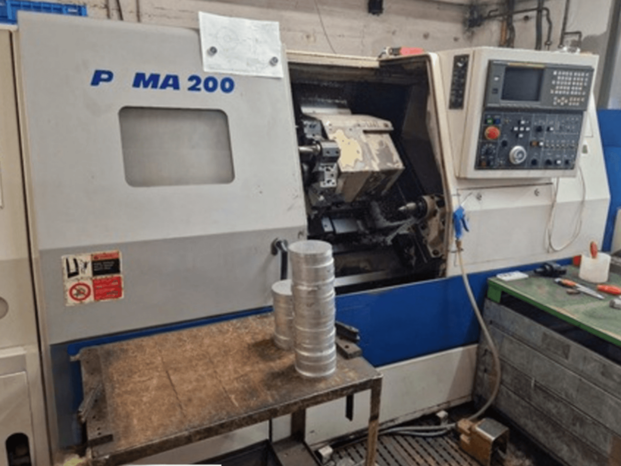 DAEWOO EcoTurn 200 horizontalios tekinimo staklės, vaizdas iš priekio, su aliuminio ruošiniais ant stalo, matomas valdymo skydelis.