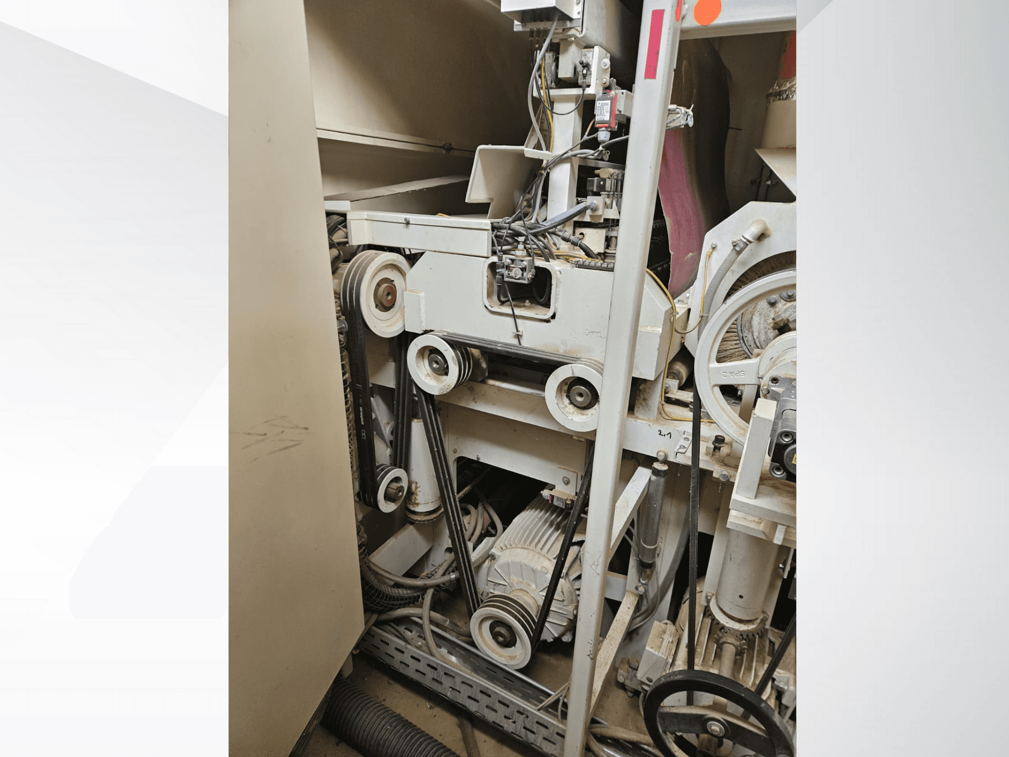 Pramoninės mašinos interjeras su diržais ir skriemuliais, variklis ir laidai, žiūrint iš šono.