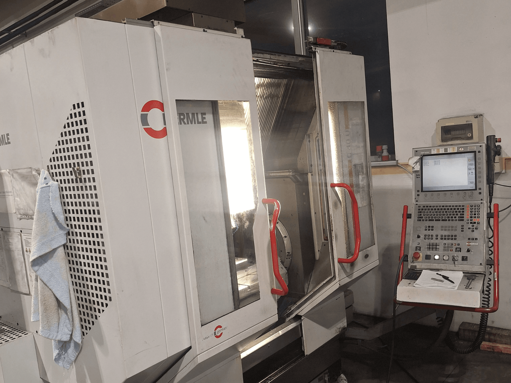 Prekės ženklo "Cormile" CNC staklės, iš priekio matomos iš dalies atidarytos durys ir valdymo skydelis su ekranu ir mygtukais.