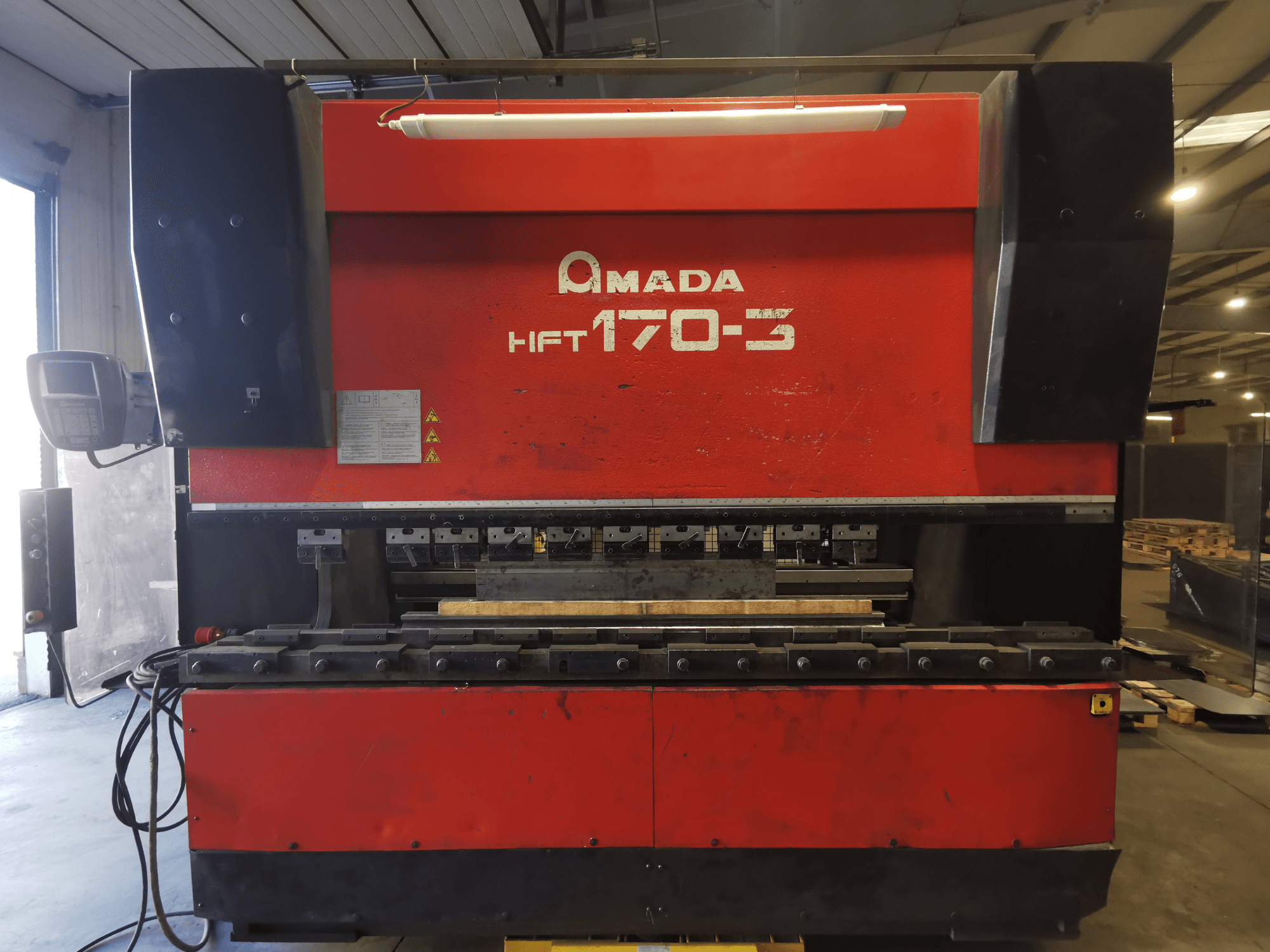 Raudonasis "Amada HFT 170-3" preso stabdys, žiūrint iš priekio, matomas valdymo skydelis, lenkimo įrankiai ir darbo paviršius.