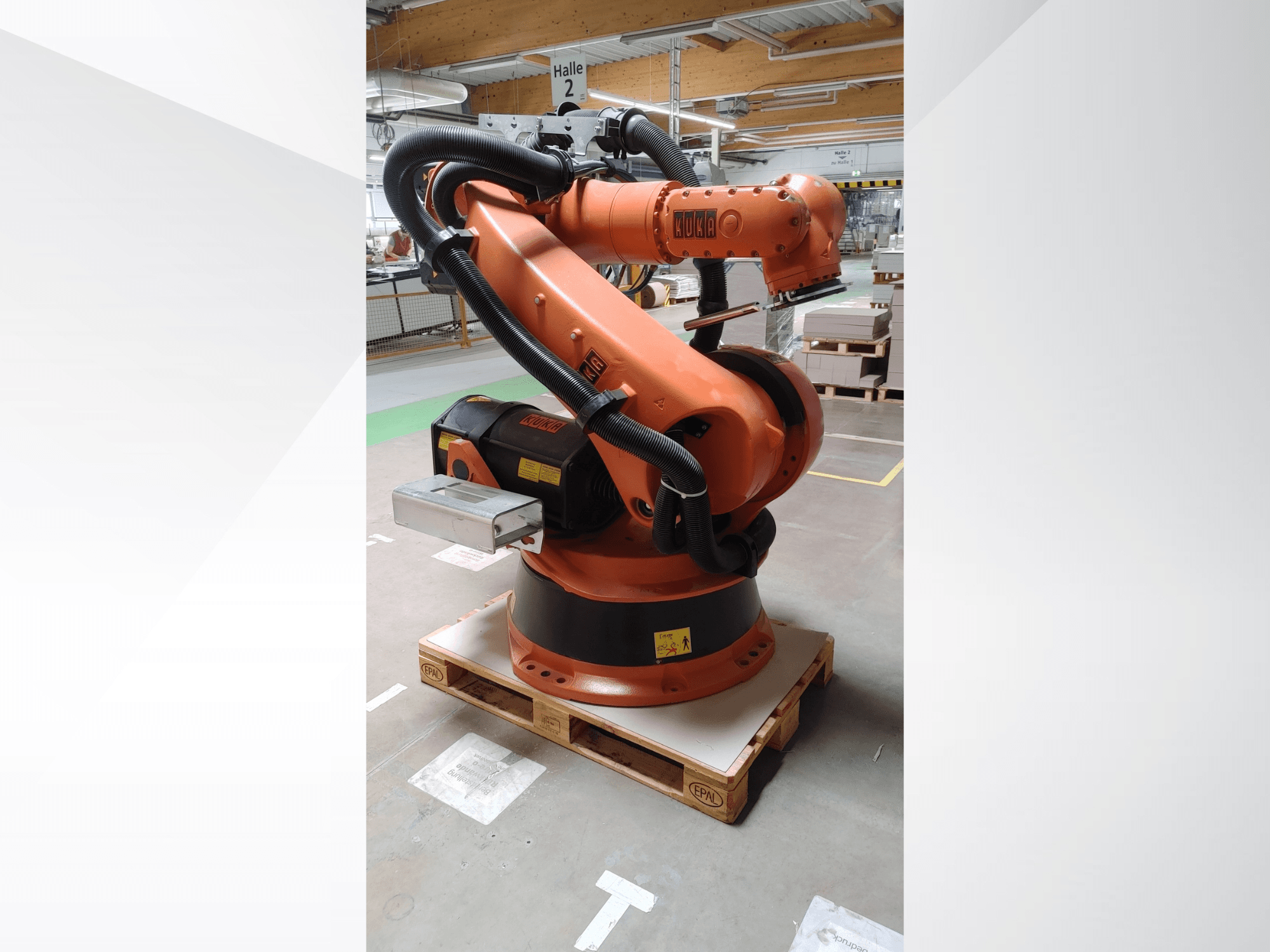 Oranžinės spalvos roboto KUKA KR140-3 COMP roboto ranka, priekinis vaizdas ant medinio padėklo, su lenkta ranka ir valdymo dėže.