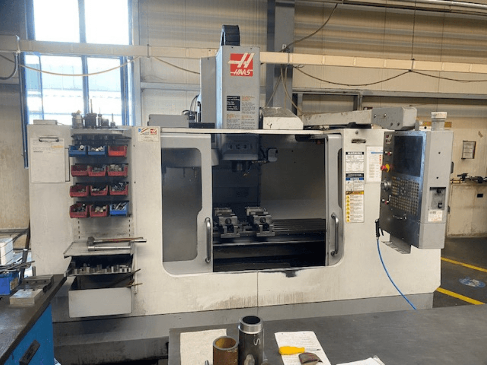 "Haas" CNC frezavimo staklių, VF-2 modelio, priekinis vaizdas, matoma įrankių laikymo vieta, valdymo skydelis ir darbo vietos įrankiai.