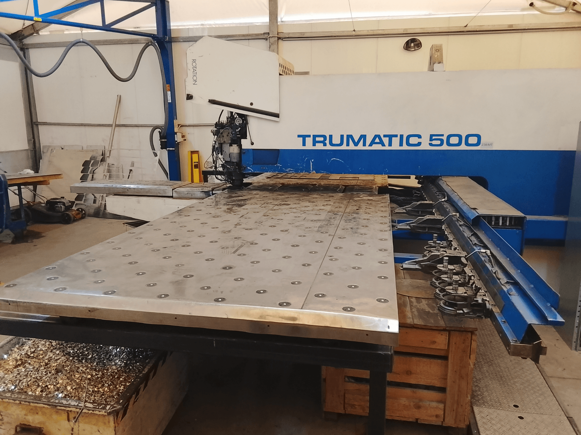 Trumatic 500 CNC staklės, vaizdas iš viršaus, didelis metalinis pjovimo stalas su pritvirtintais įrankiais ir drožlėmis.