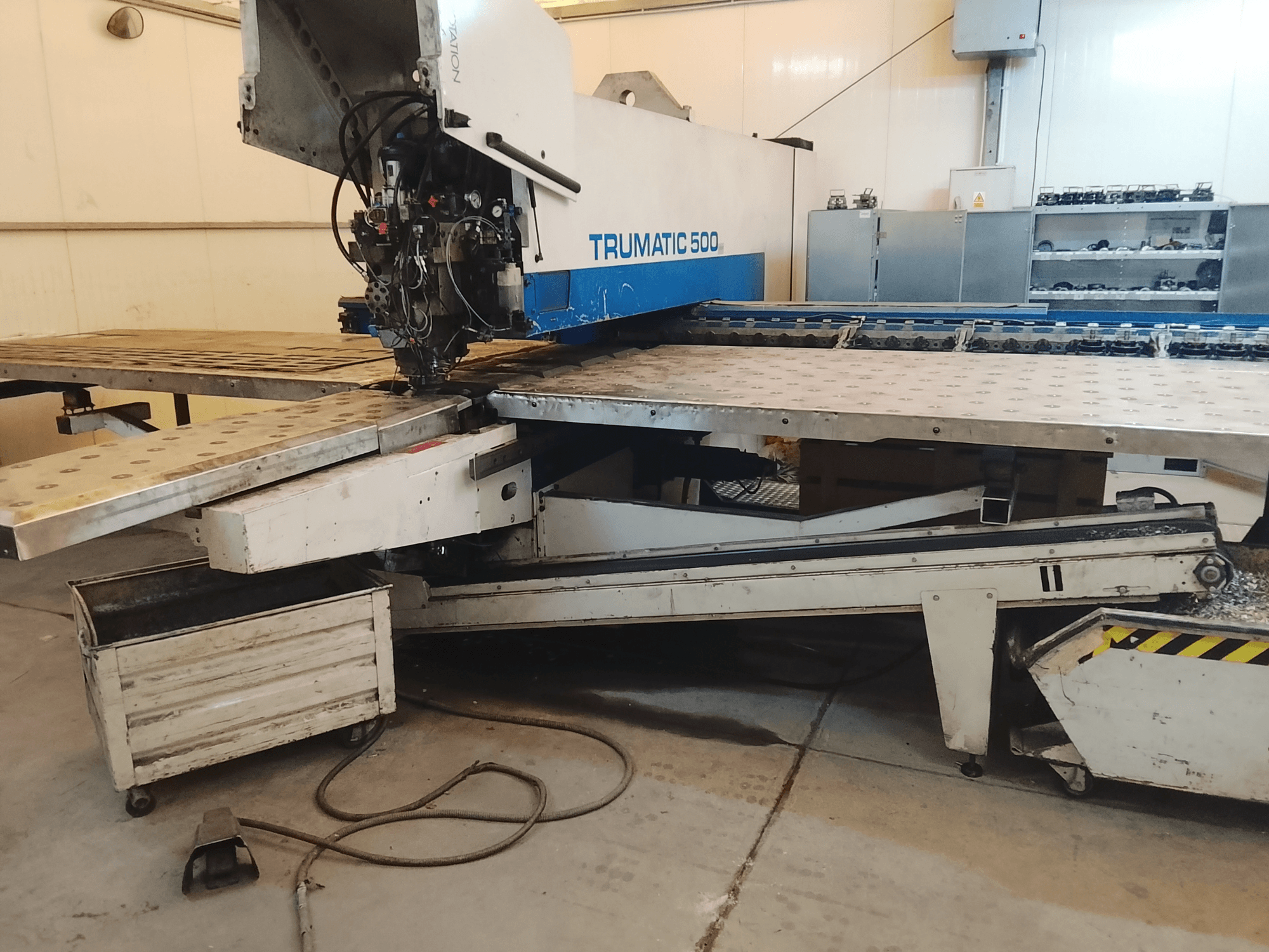 TRUMATIC 500 CNC staklės dirbtuvėse, šoninis vaizdas, rodantis pjovimo galvutę ir metalinį stalą su iš anksto išgręžtomis skylėmis.