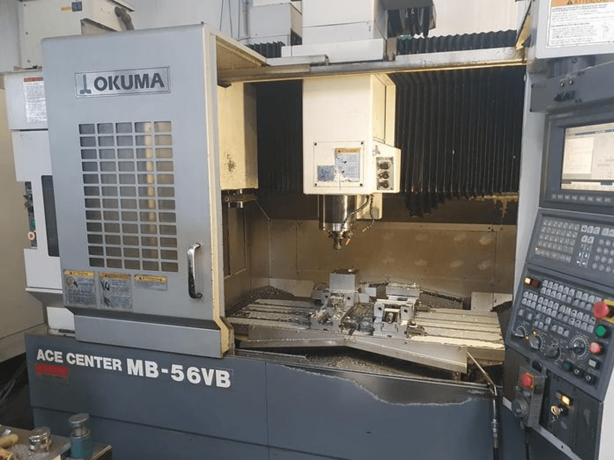 Okuma ACE CENTER MB-56VB CNC frezavimo staklės iš priekio, kuriose matomas valdymo skydelis ir apdirbimo zona.