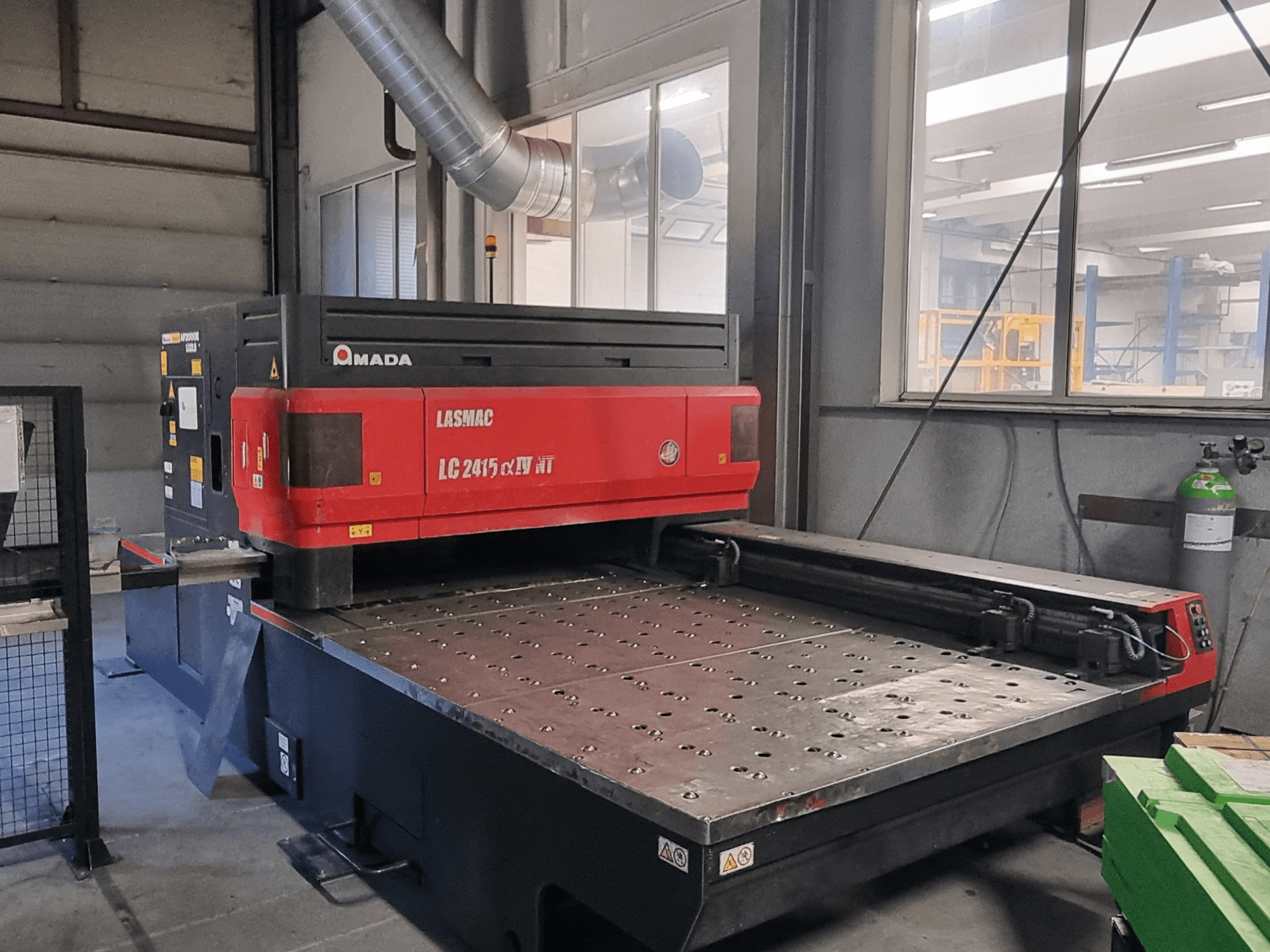 "Amada LASMAC LC 2415 αⅡ NT" raudonos ir juodos spalvų lazerinio pjovimo staklės su pjovimo lova ir tiksliu valdymu, vaizdas iš priekio.