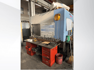 "Doosan" apdirbimo centras su raudonu darbo stalu ir saugykla, kurioje rodomi įrankiai ir įranga, žiūrint iš priekio.