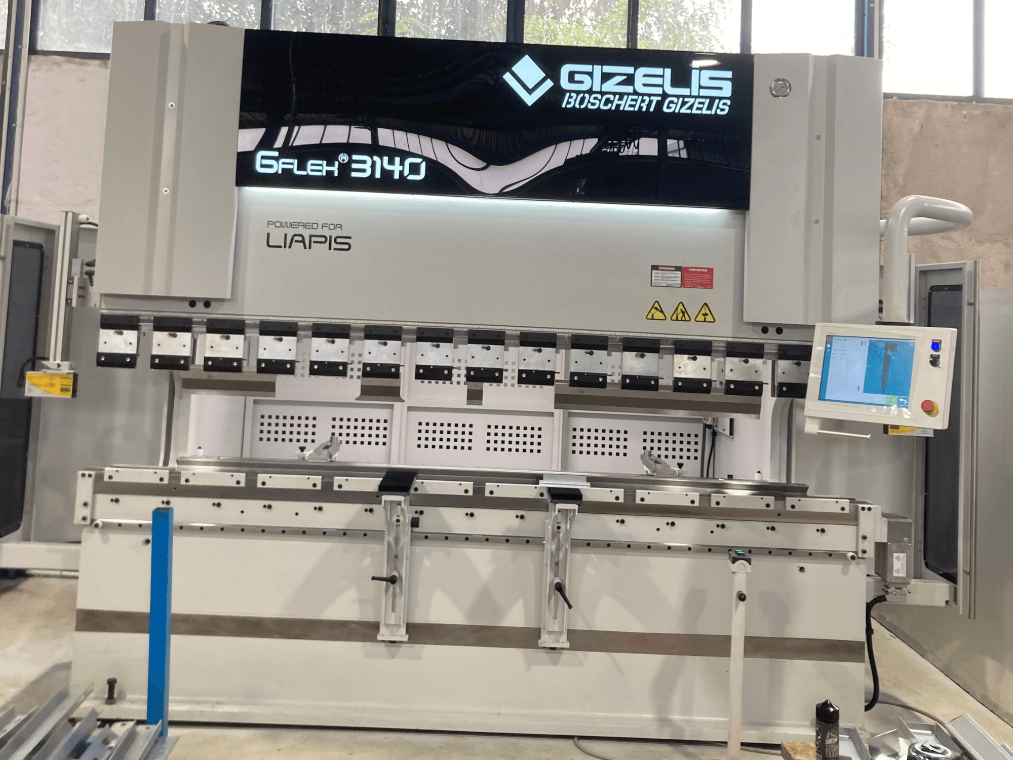 Hidraulinis presas GIZELIS G-FLEX 3140 iš priekio su valdymo ekranu, kuriame yra daugybė lenkimo įrankių ir saugos ženklų.