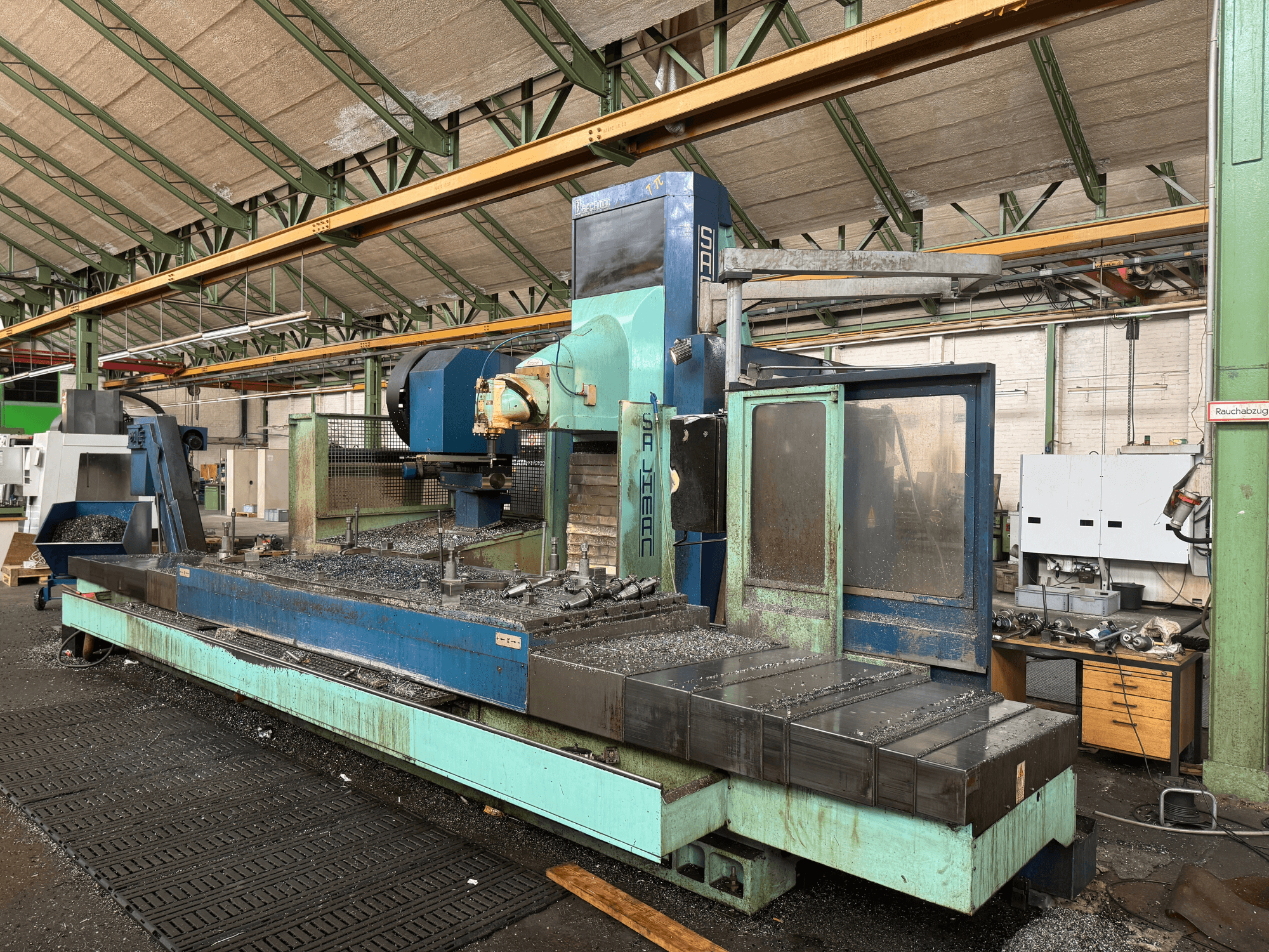 Frezavimo staklės "Salvador" gamykloje, vaizdas iš priekio, mėlynos ir žalios spalvos, matomos metalo drožlės ant lovio.