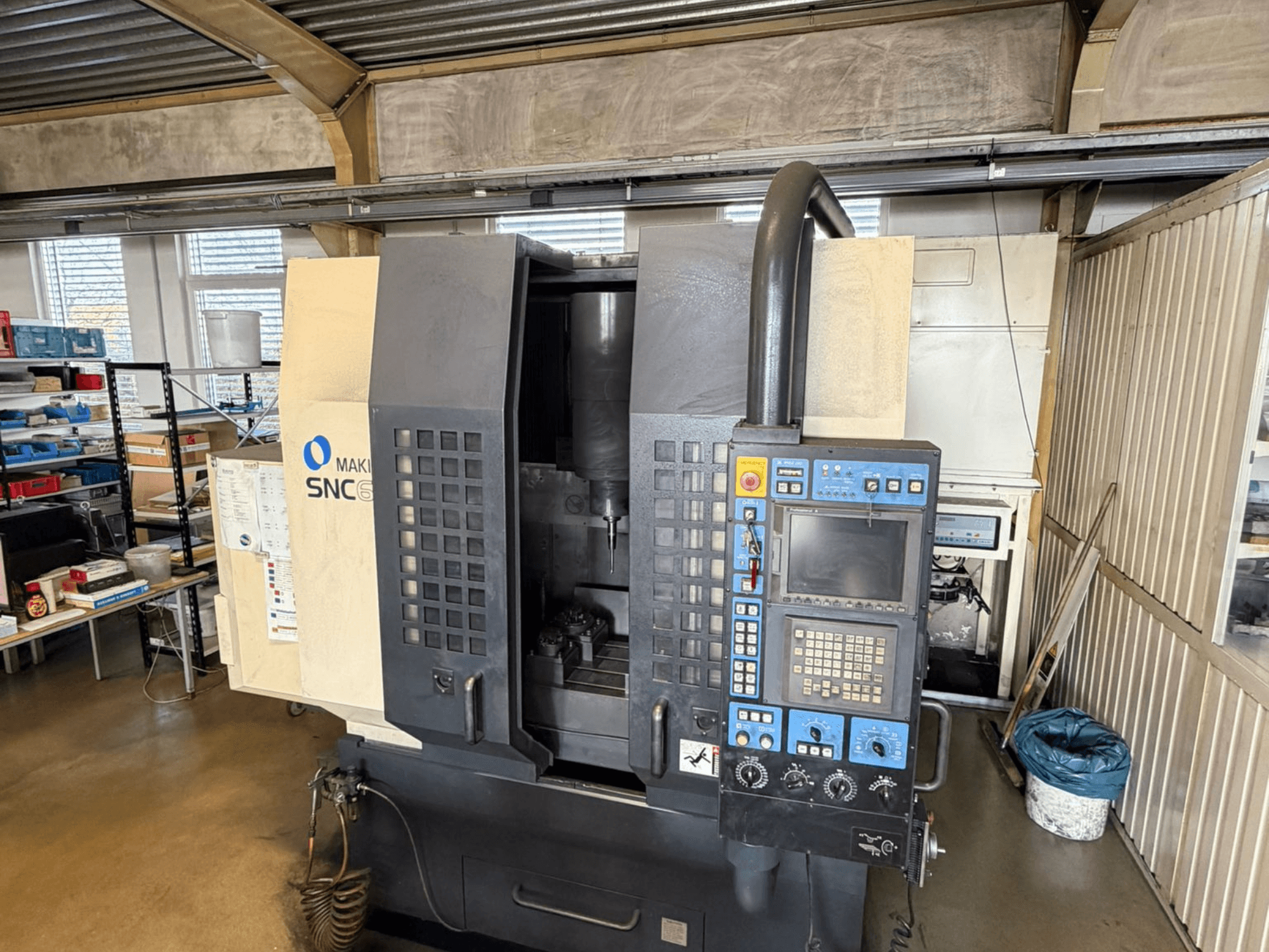 Vertikalaus apdirbimo centro "Makino SNC 64-A15" priekinis vaizdas, kuriame matomas valdymo skydelis, apdirbimo zona ir pramoninė darbo vieta.
