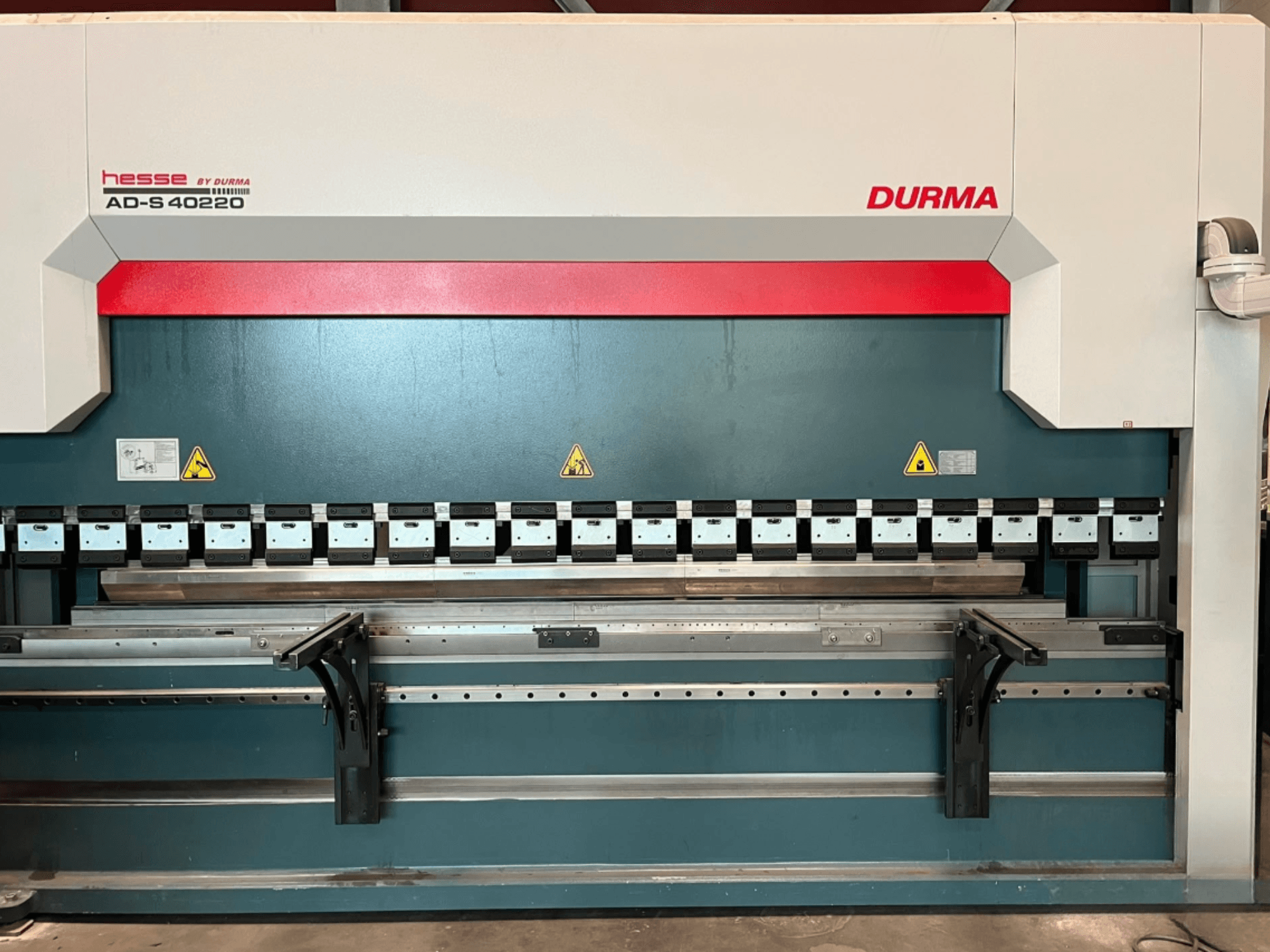 „Durma AD-S 40220“ presinis lenkimo staklės, matomos iš priekio, su įvairiais lenkimo įrankiais ir saugos etiketėmis.