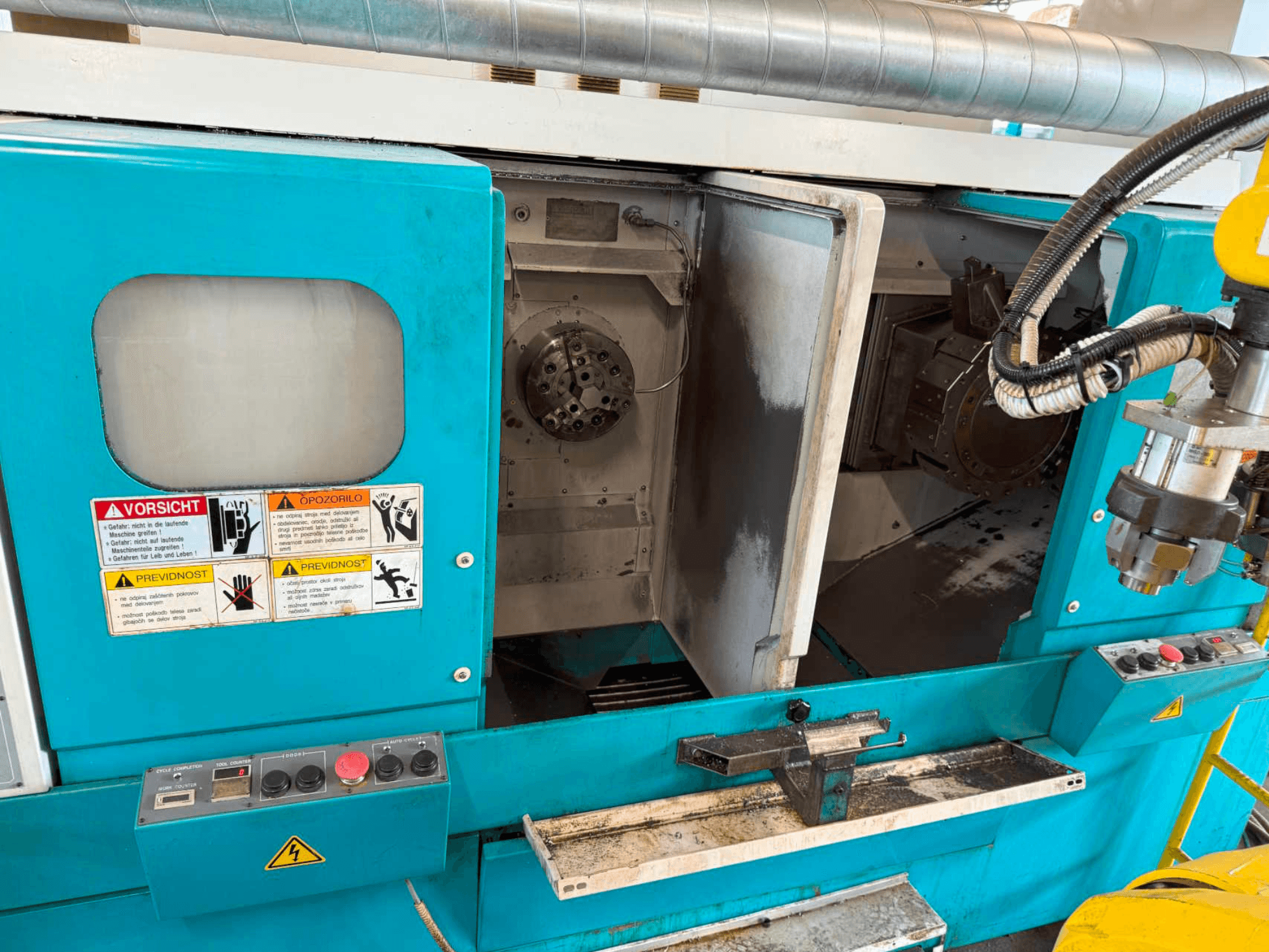 Horizontaliosios tekinimo staklės DOOSAN H310T, priekinis vaizdas, kuriame matomas valdymo skydelis ir verpstės zona su saugos įspėjimais.