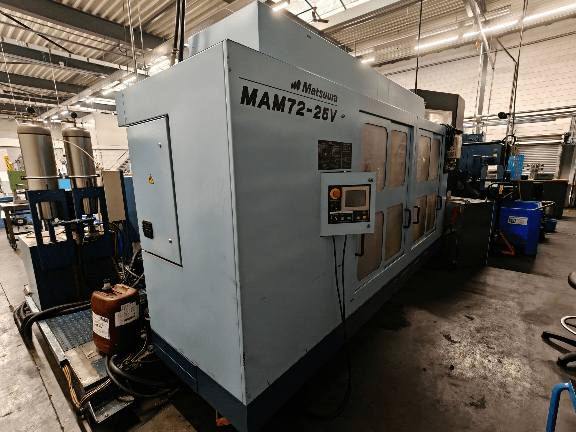 Matsuura MAM72-25V CNC staklės, vaizdas iš šono, su valdymo skydeliu, dviem aušinimo skysčio rezervuarais ir darbo vieta pramoninėje aplinkoje.