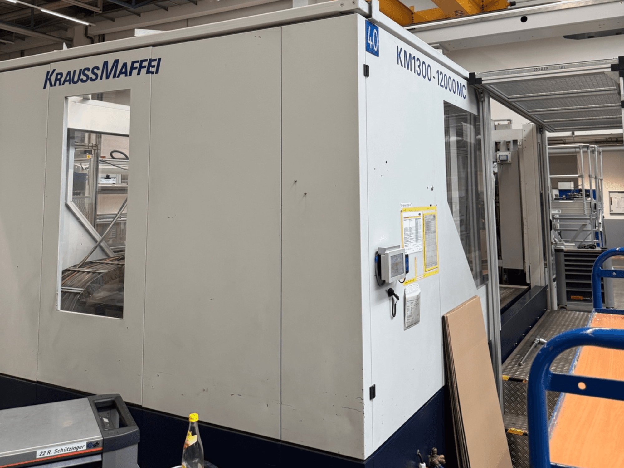 "Krauss Maffei" hidraulinės įpurškimo liejimo mašinos KM1300-12000 MC, šoninis vaizdas, matomas valdymo skydelis ir darbinė erdvė.