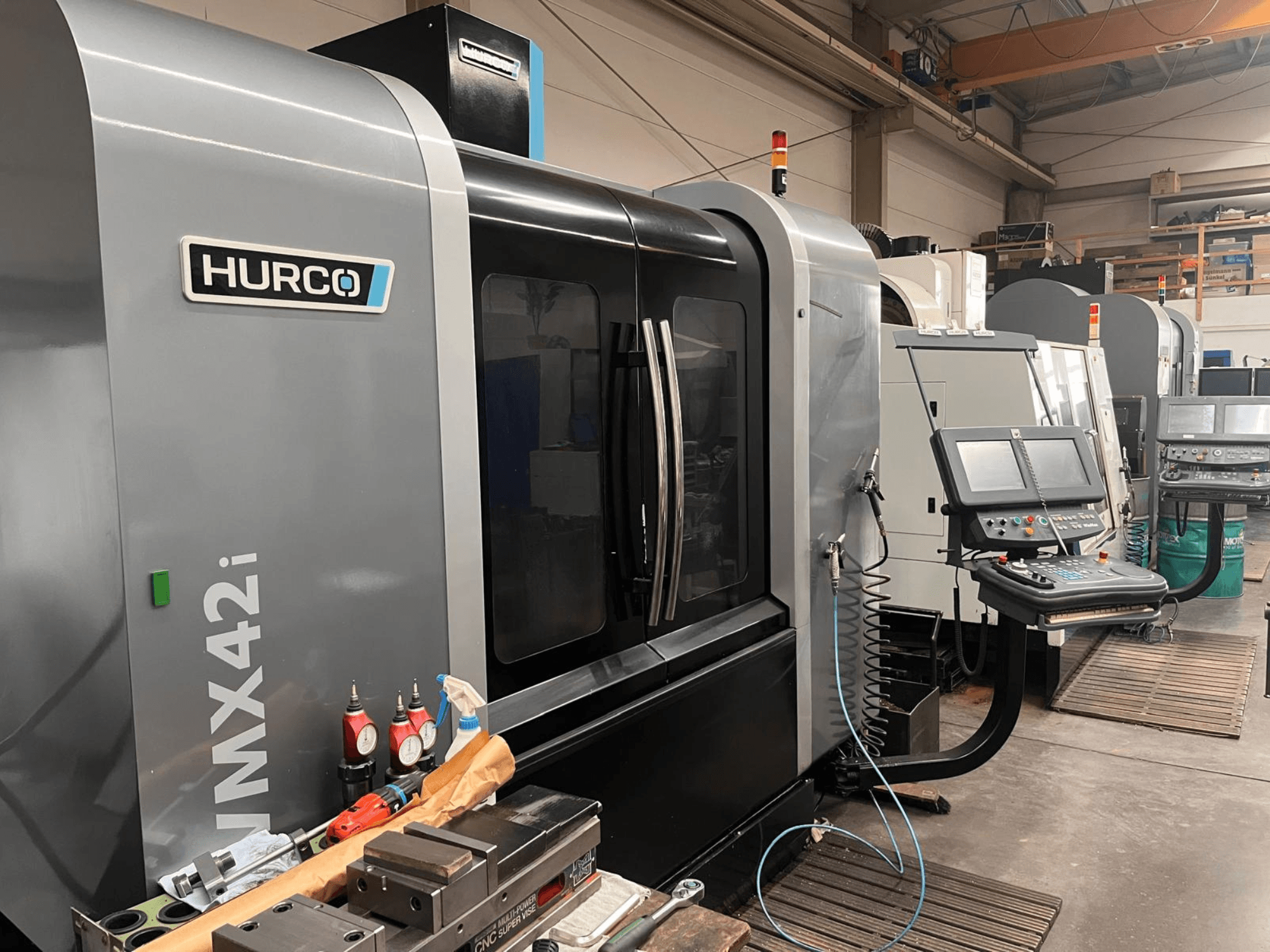 Hurco VMX42i CNC staklės dirbtuvėse, vaizdas iš priekio, valdymo skydelis ir įvairūs įrankiai ant darbo stalo.