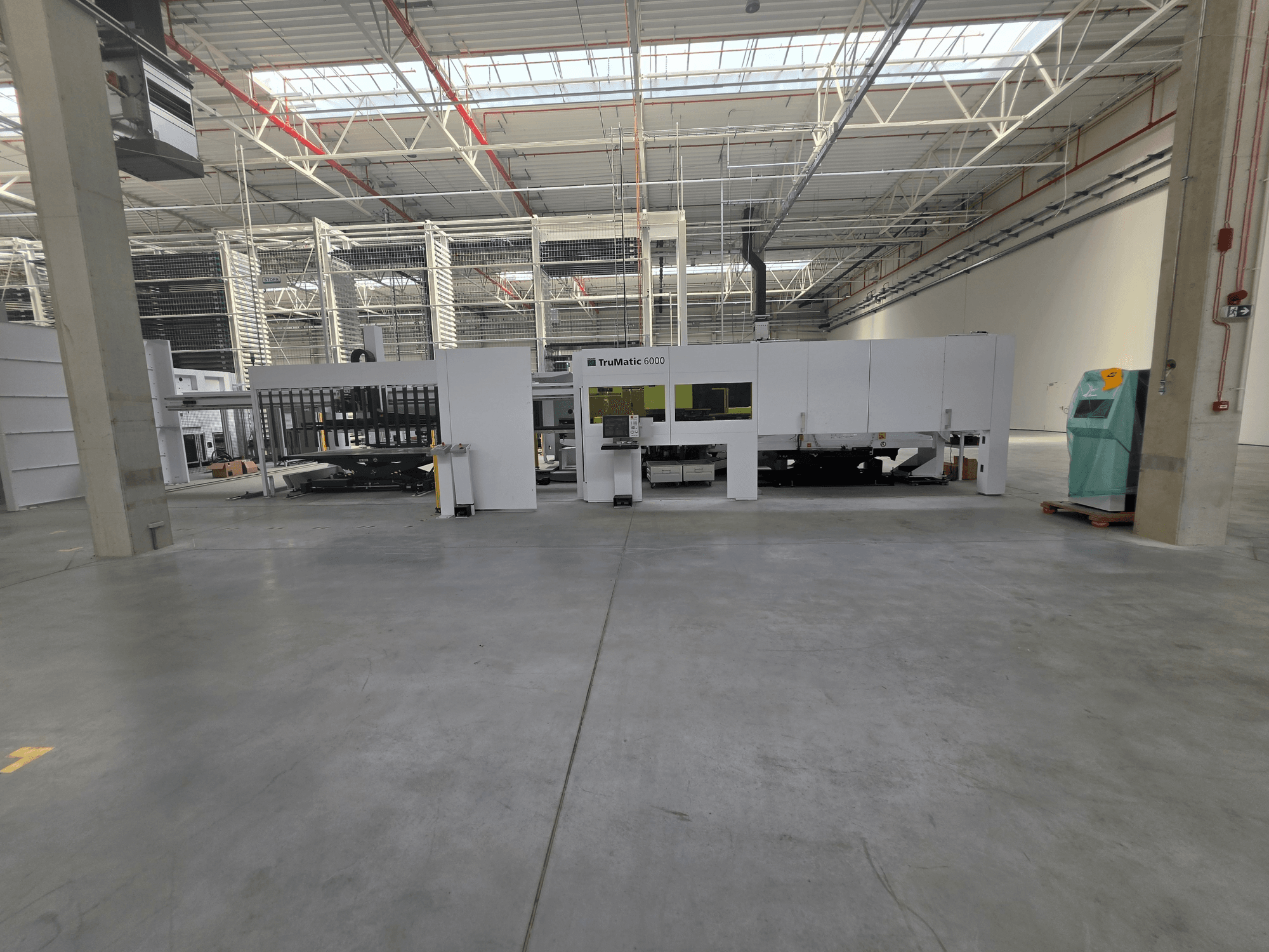 „TRUMPF TruMatic 6000-1600“ pluošto šlifavimo ir lazerinio pjovimo kombinuotas staklės erdviame sandėlyje, vaizdas iš priekio.