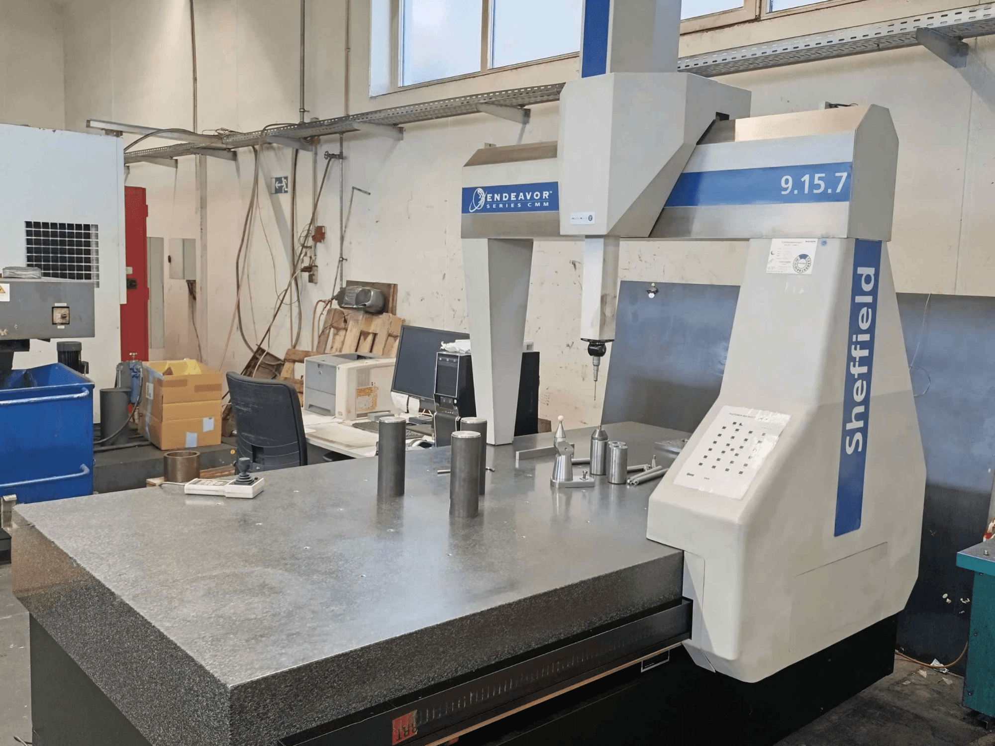 Koordinatinės matavimo staklės "Sheffield Endeavor 9.15.7" dirbtuvėse su granitiniu stalu ir metaliniais ruošiniais.