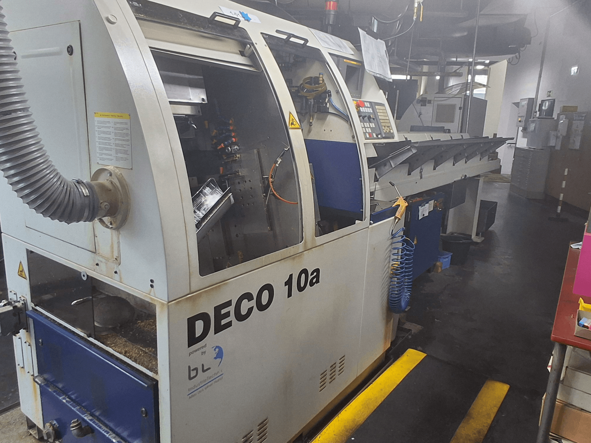 Šveicariško tipo tekinimo staklės TORNOS DECO 10a, vaizdas iš priekio; turi valdymo skydelį, matomus mechanizmus ir dulkių ištraukimo vamzdį.