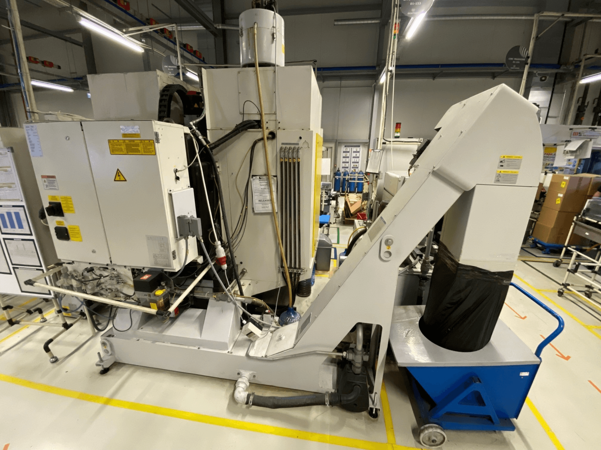 „FANUC ROBODRILL α-D21LiB“ vertikaliojo apdirbimo centro vaizdas iš priekio, kuriame matomi elektriniai komponentai ir išmetimo latakas.