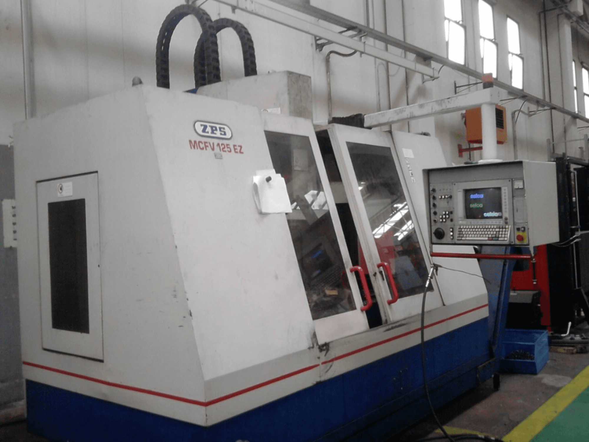 ZPS MCFV 125 EZ CNC staklės, vaizdas iš priekio su valdymo skydeliu ir raudonomis rankenomis, dirbtuvėse, matomos žarnos.