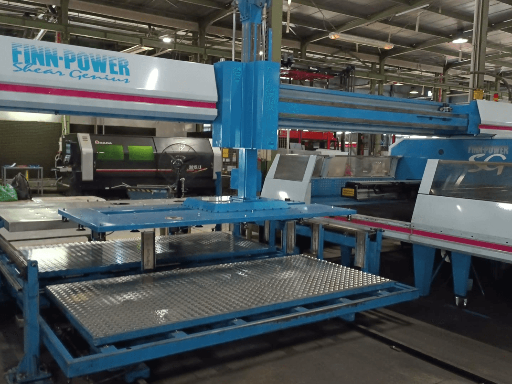„Finn-Power SG6 Shear Genius“ CNC štampavimo staklių vaizdas iš priekio, kuriame matomi metaliniai stalai ir konstrukcinės ypatybės.