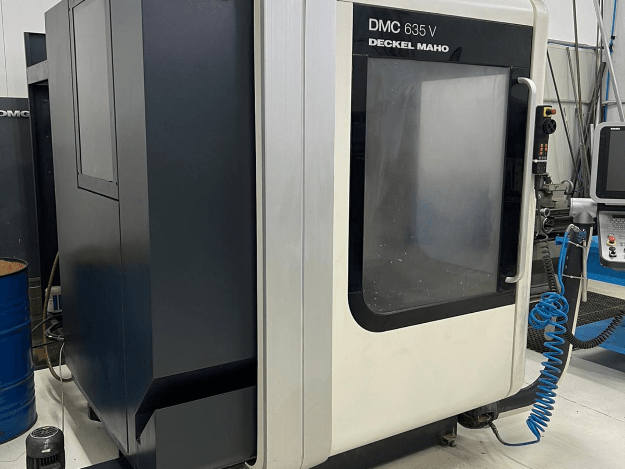 Deckel Maho frezavimo staklės DMC 635 V, šoninis vaizdas, kuriame matyti valdymo skydelis ir iš dalies atidarytos prieigos durys.