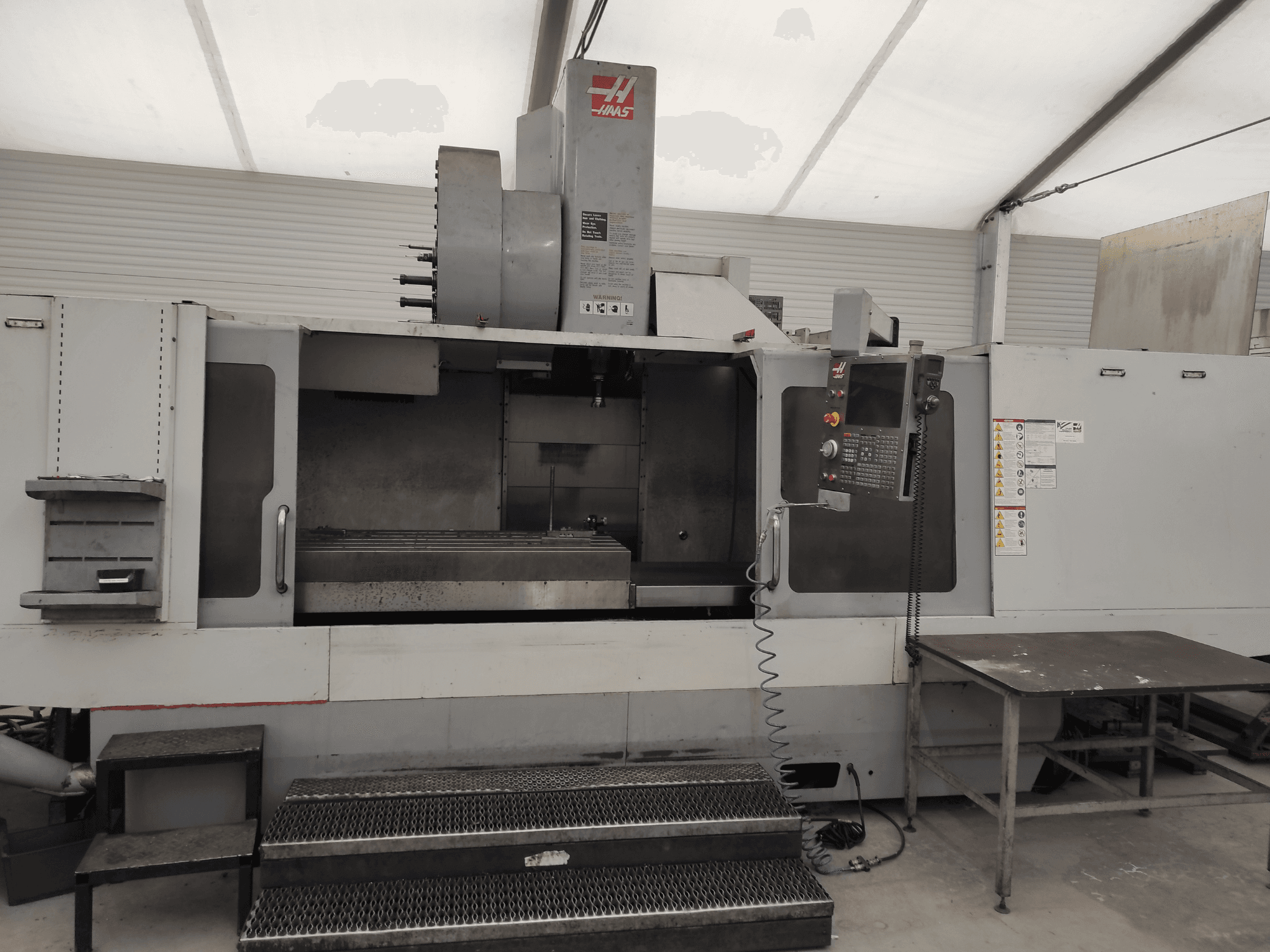 HAAS VF-10/50HE vertikalusis apdirbimo centras, priekinis vaizdas, kuriame matyti valdymo skydelis, staklių lova ir prieinamas valdymo laiptelis.