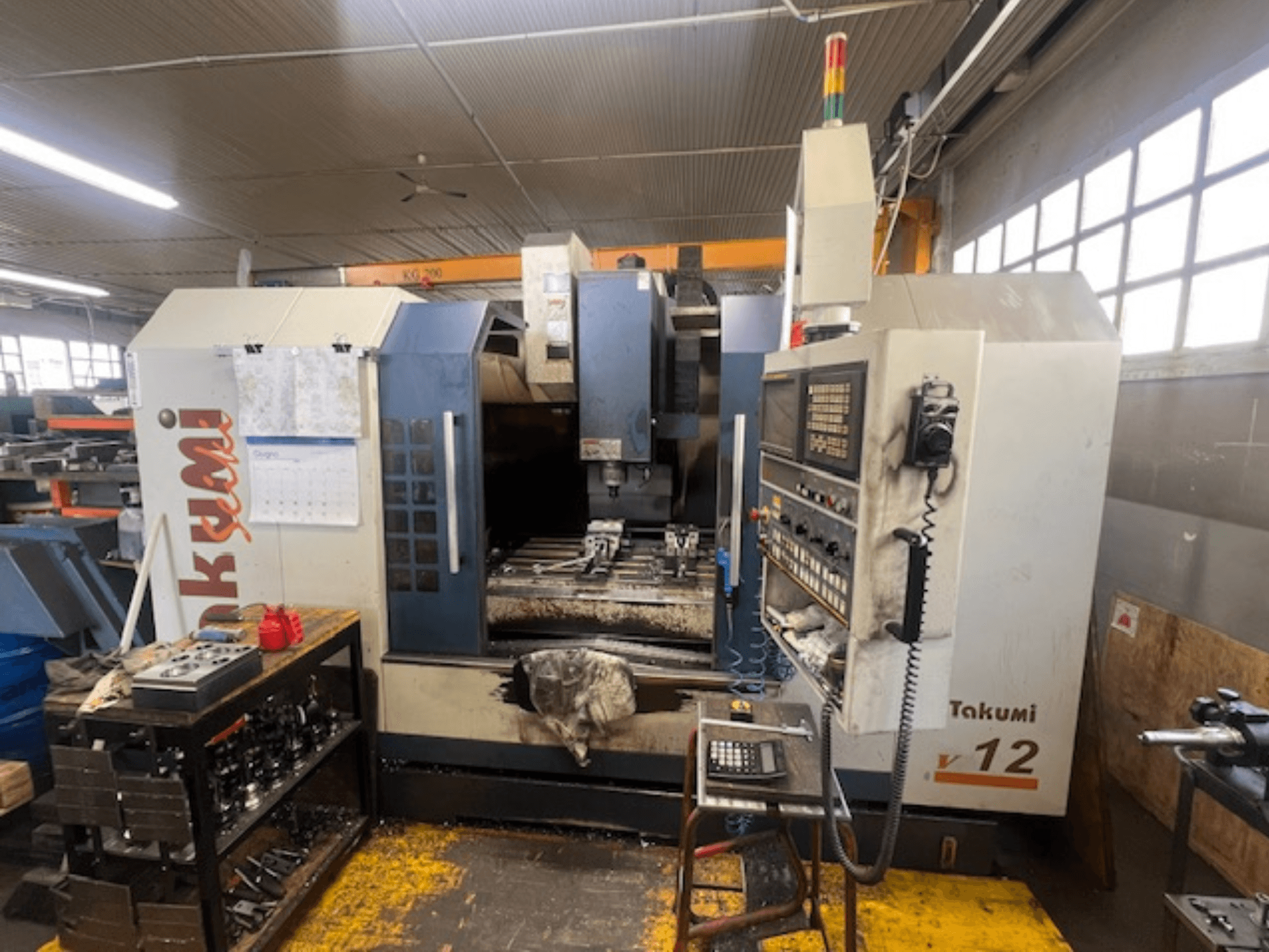 CNC frezavimo staklės "Takumi V12 CNC" iš šono, kuriame matyti valdymo skydelis, pjovimo zona ir darbo vietoje esantys įrankiai.