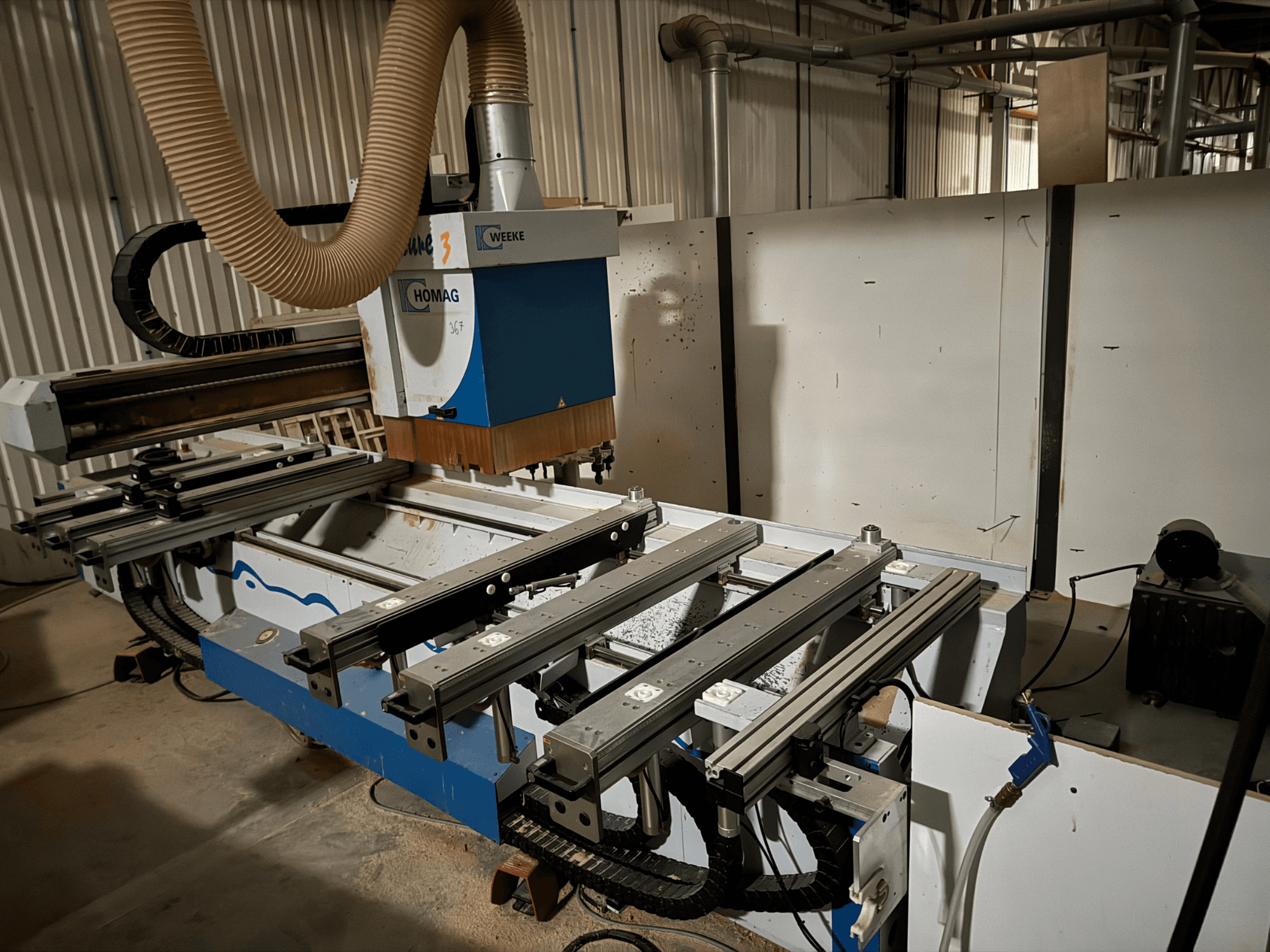 HOMAG CNC staklės su mėlynos ir baltos spalvų dizainu, vaizdas iš šono, turi slankiojančius bėgius, dulkių nusiurbimo sistemą ir pritvirtintus įrankius.