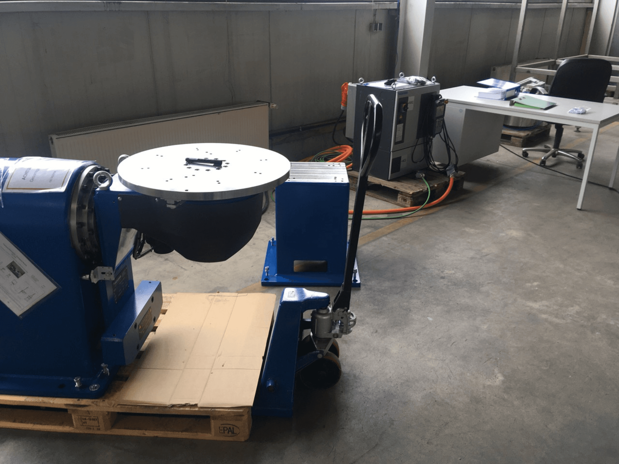 Mėlyna pramoninė įranga su apvaliu pagrindu ir valdymo skydeliu, žiūrint iš priekio, ant medinio padėklo biure.