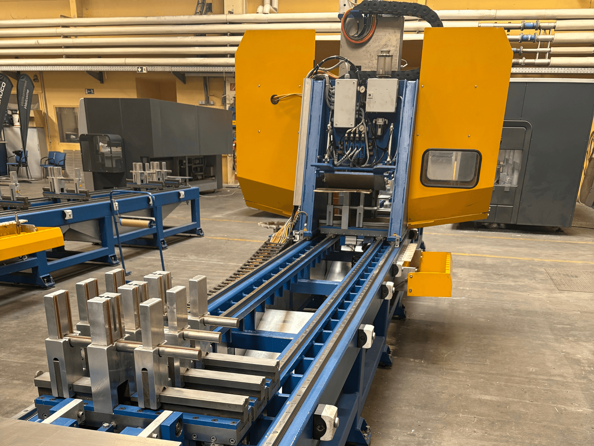 SCHÜCO PBX AL universalaus apdirbimo centro vaizdas iš priekio, kuriame ant mėlyno apdirbimo stalo demonstruojamos metalinės detalės.