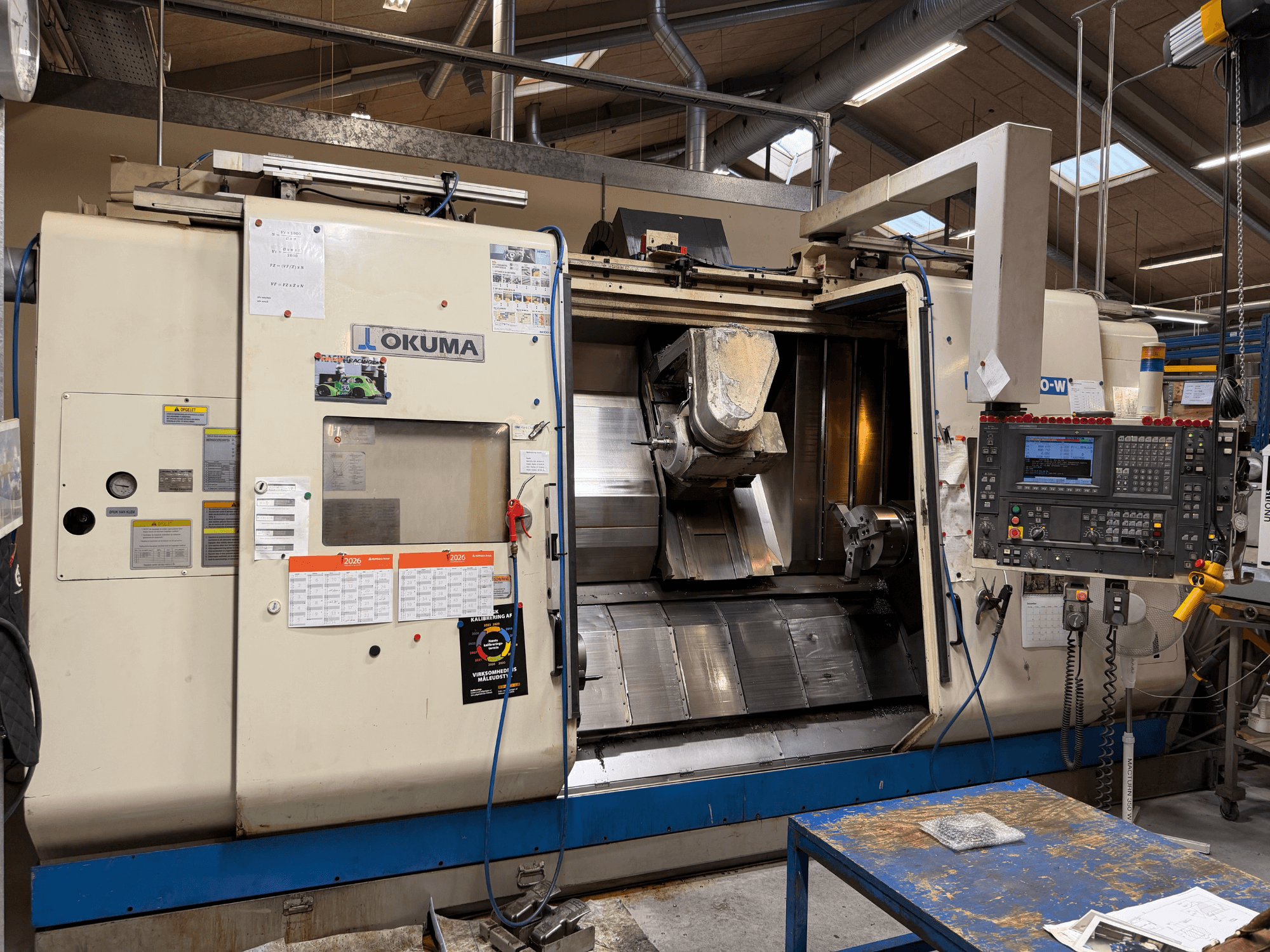 „Okuma MacTurn350-W“ tekinimo ir frezavimo centras, vaizdas iš priekio, kuriame matomas valdymo pultas ir atviras priėjimas prie apdirbimo zonos.