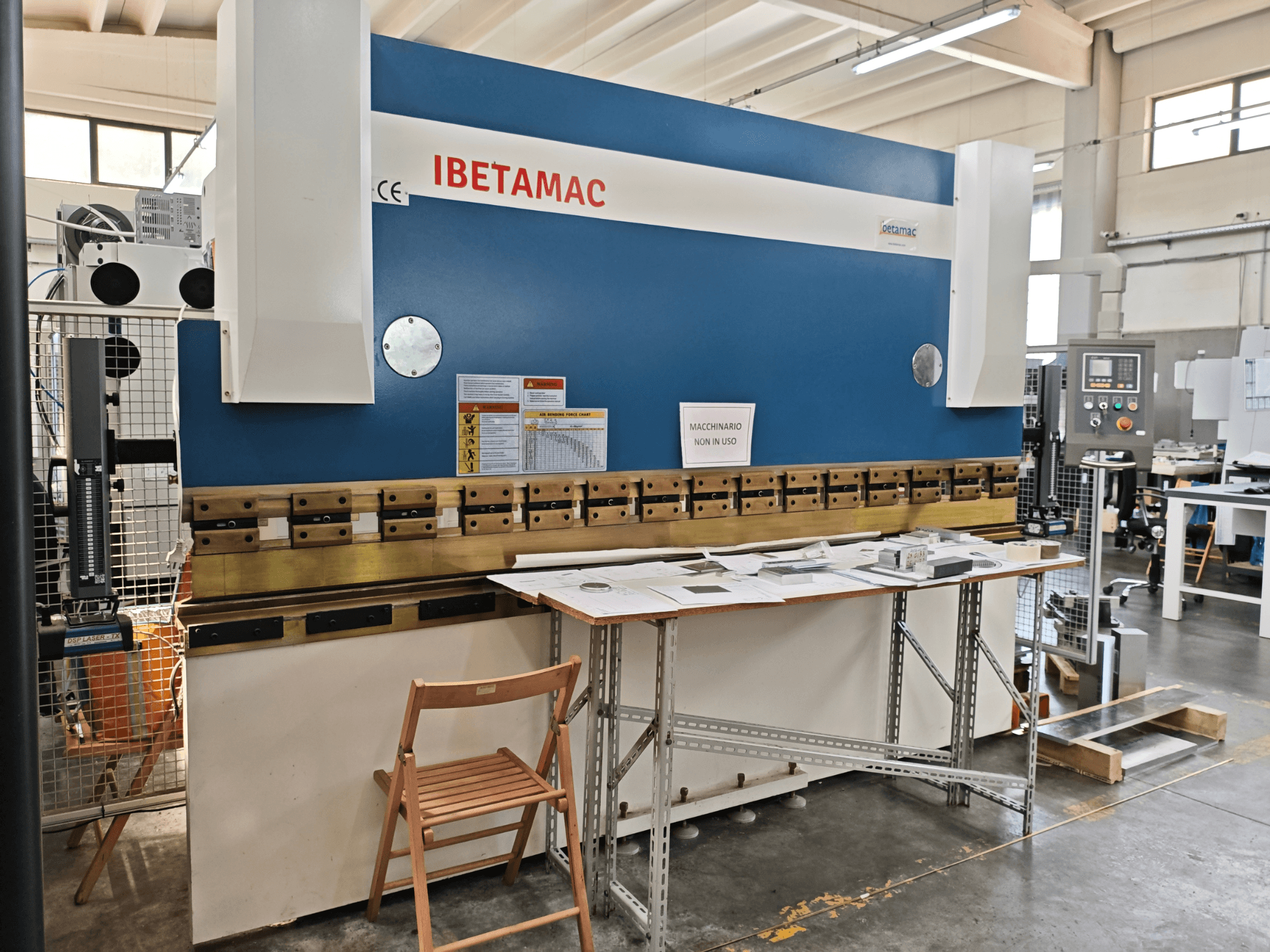 „IBETAMAC 3200 100T“ lenkimo presas dirbtuvėse, šoninis vaizdas, kuriame matomas valdymo pultas, darbo zona ir saugos nurodymai.