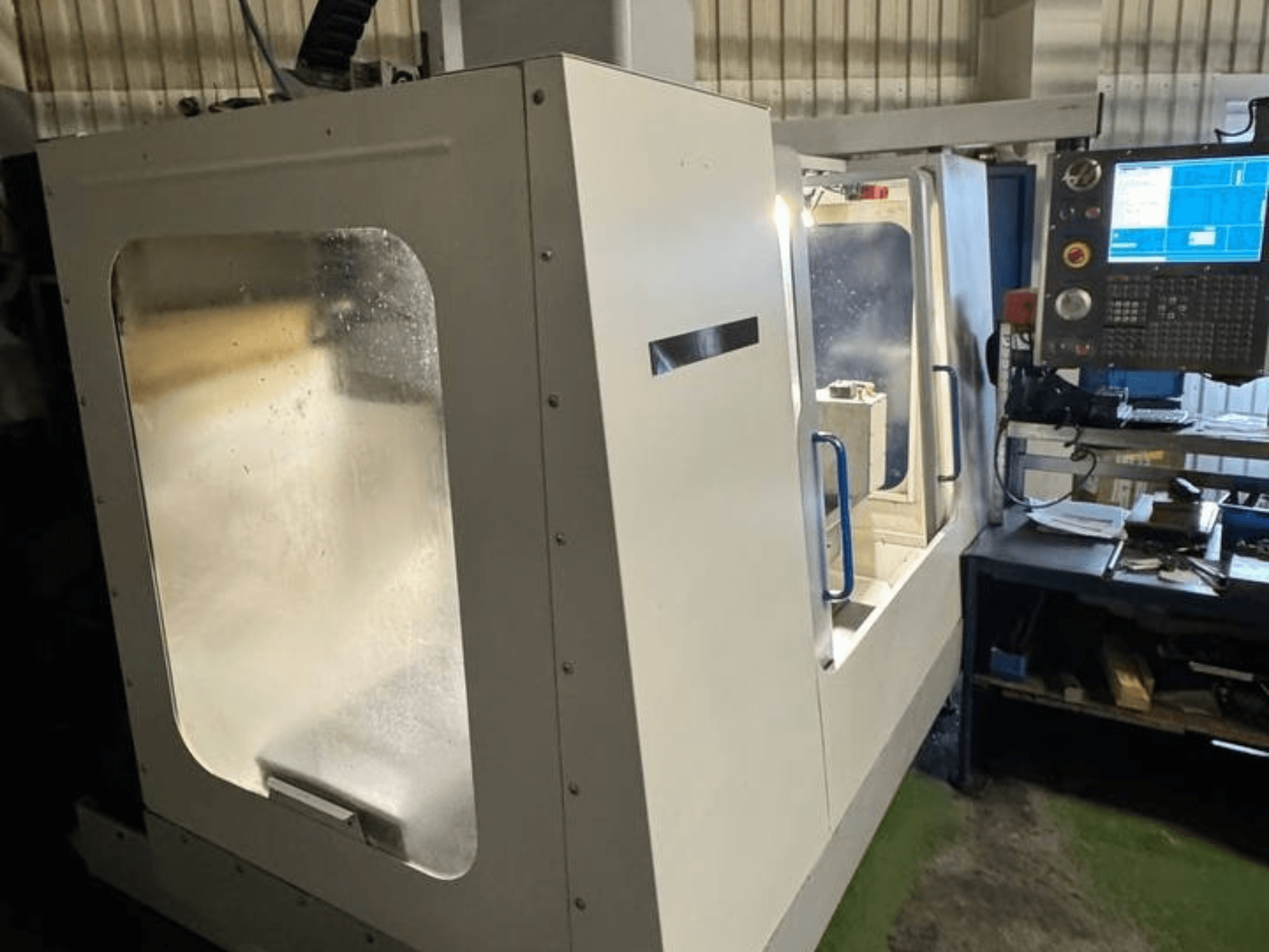 HAAS VCE 750 vertikalusis apdirbimo centras iš šono, su valdymo skydeliu ir skaidriu apsauginiu gaubtu.