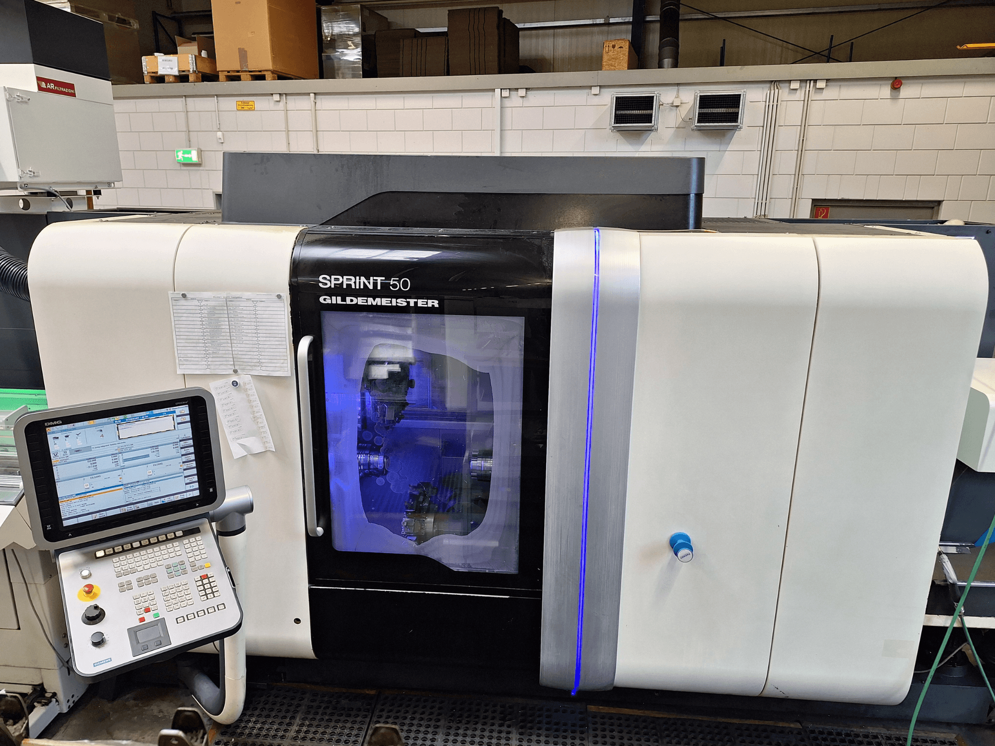 DMG Sprint 50 2T horizontalios tekinimo staklės, vaizdas iš priekio, su valdymo skydeliu ir permatomu korpusu, iš kurio matyti viduje esančios mašinos.