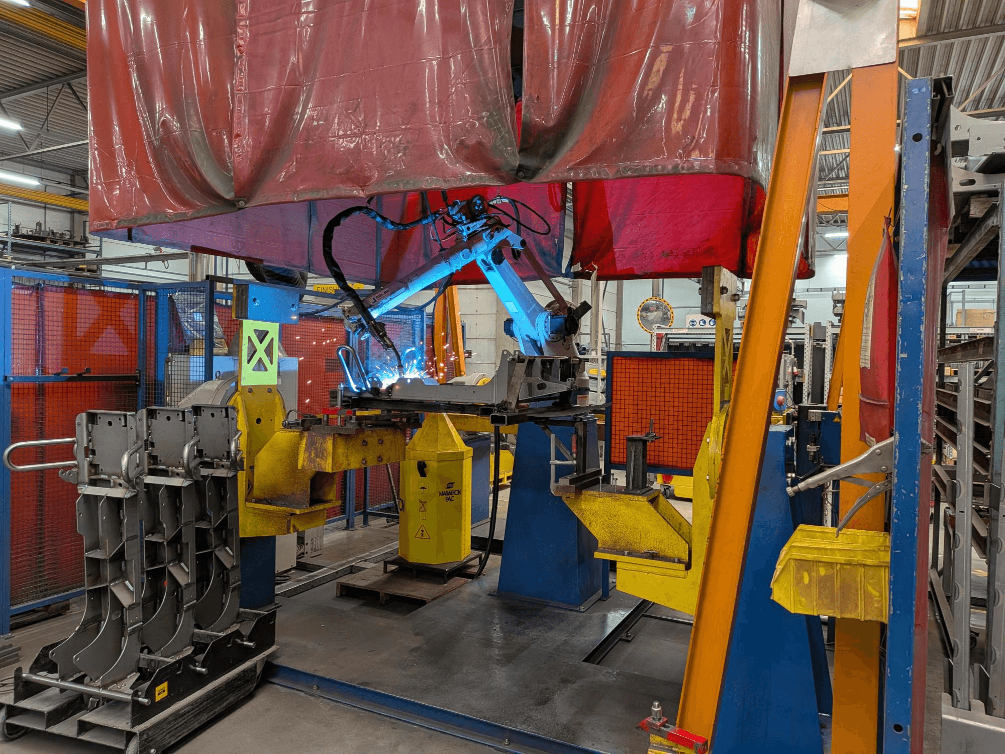Suvirinimo robotas „OTC Daihen DR4200“ darbo metu, vaizdas iš priekio, su ryškiai mėlyna suvirinimo lanku ir apsauginiu gaubtu.