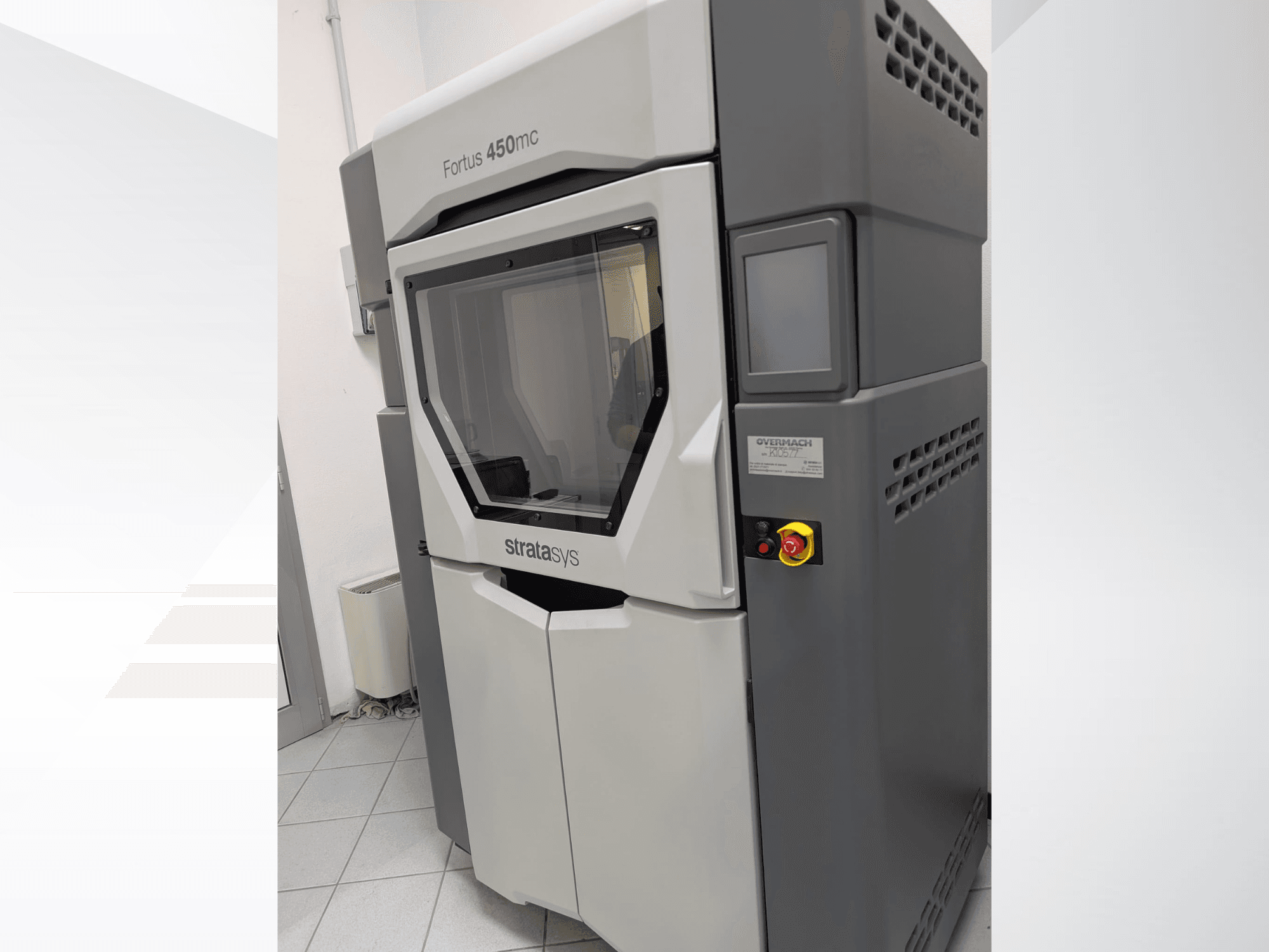 Plastikinis 3D spausdintuvas "Fortus 450mc" su skaidriu priekiniu skydeliu ir šone esančiais valdymo mygtukais.