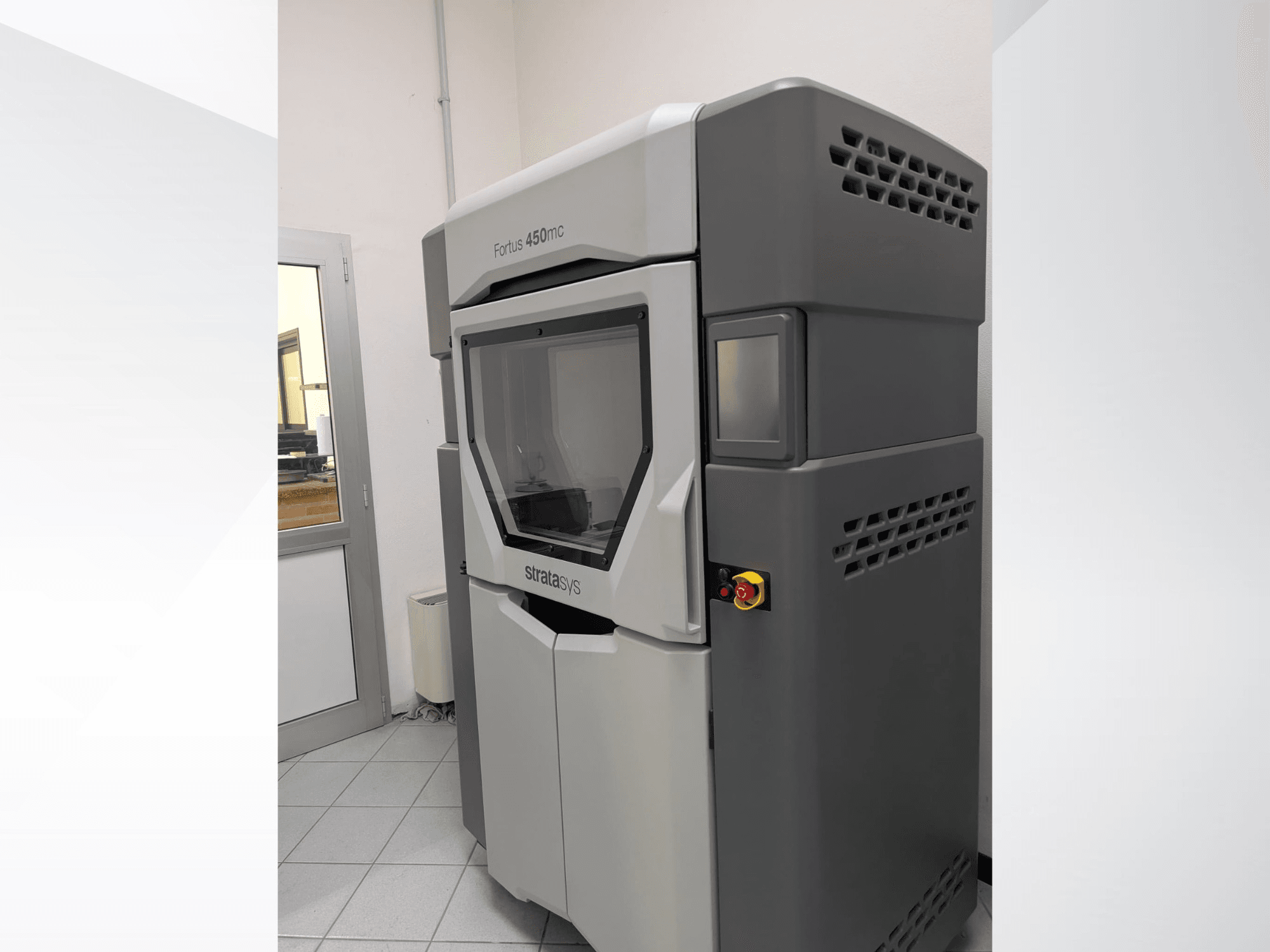 Plastikinis 3D spausdintuvas "Stratasys FORTUS 450mc" iš šono, kuriame matyti aptakus dizainas ir valdymo skydelis.