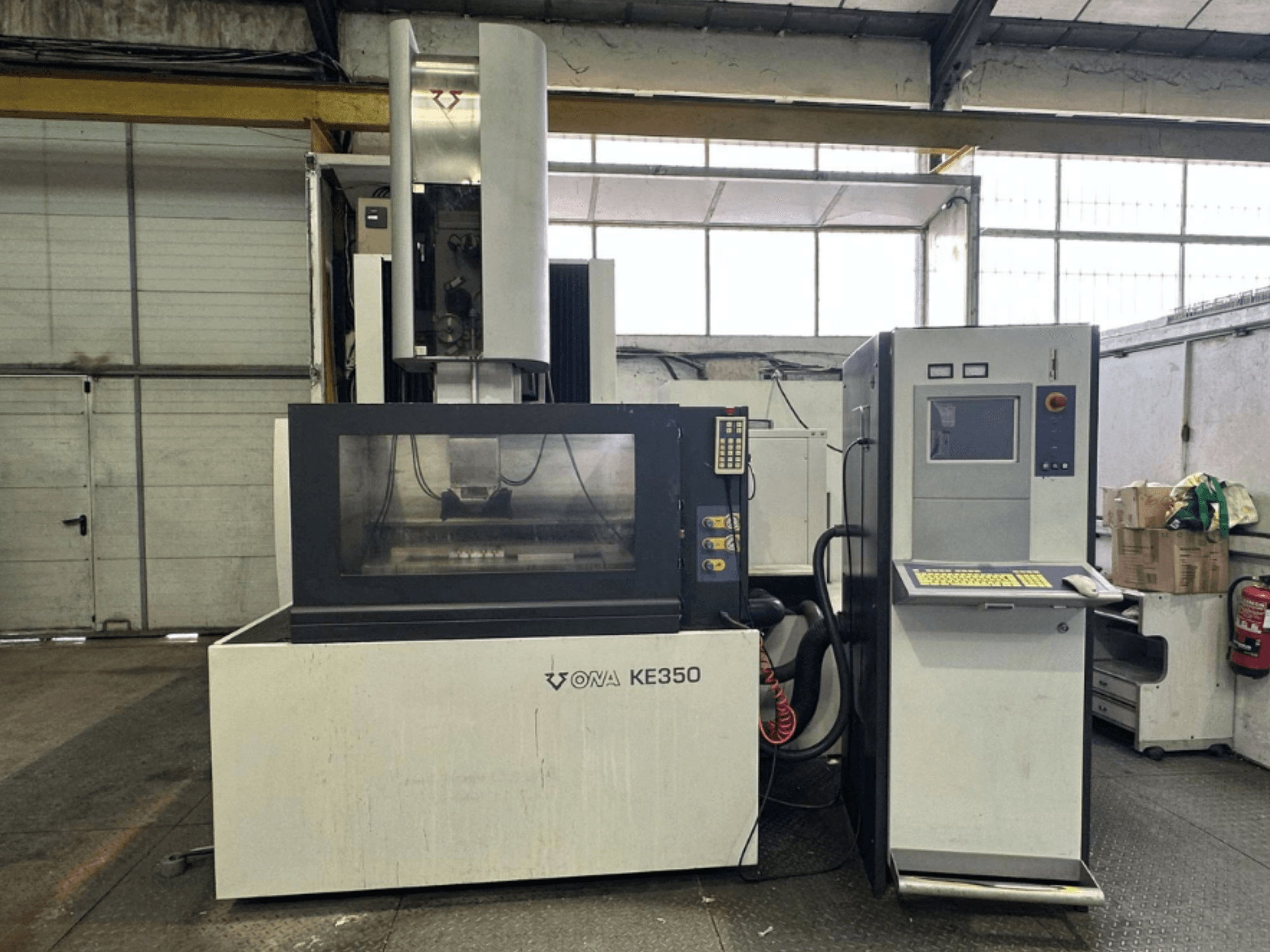 ONA KE350 CNC staklių su valdymo skydeliu, ekranėliu ir įvairiais mygtukais vaizdas iš priekio pramoninėje aplinkoje.